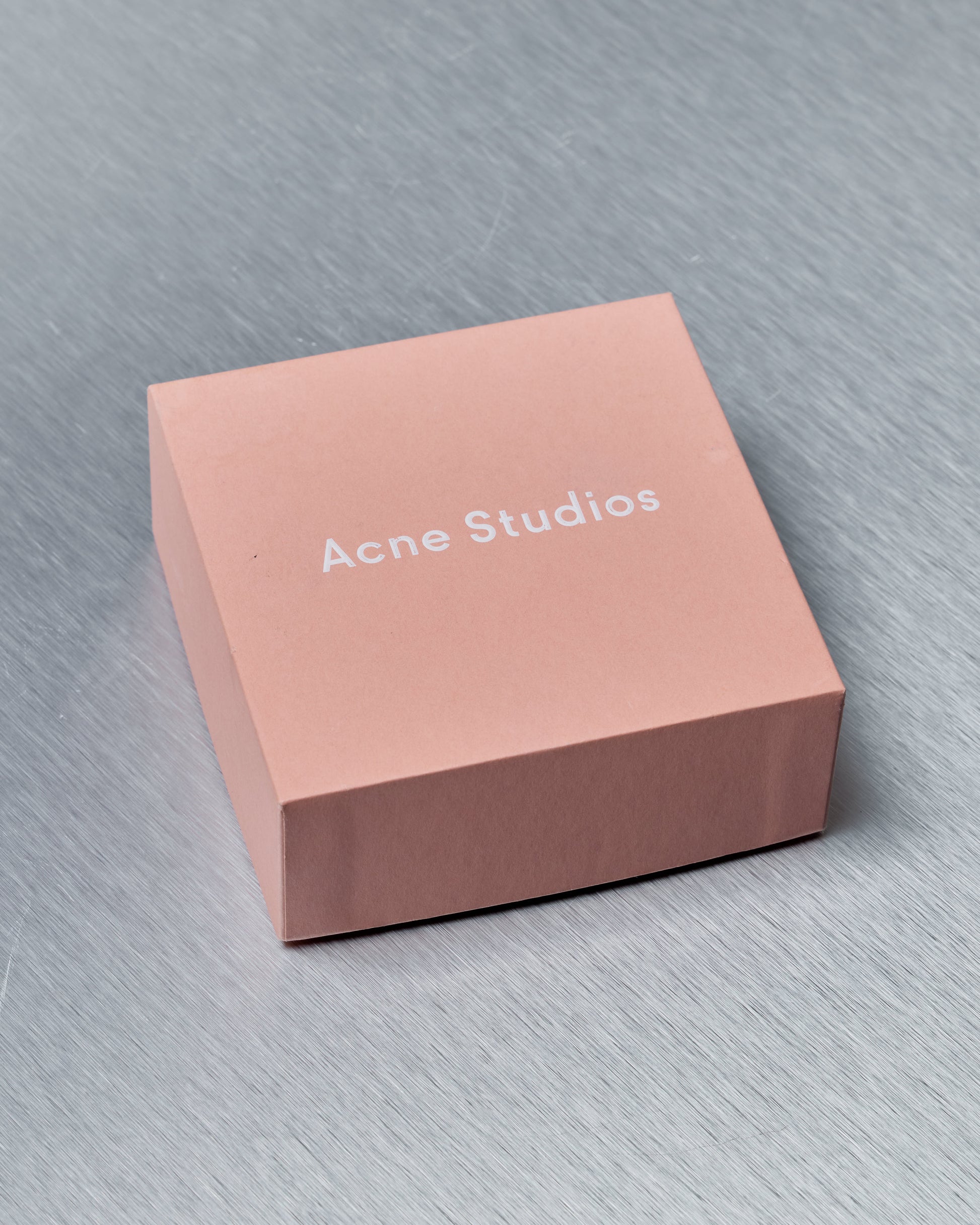 Pink 'Acne Studios' box on a gray surface