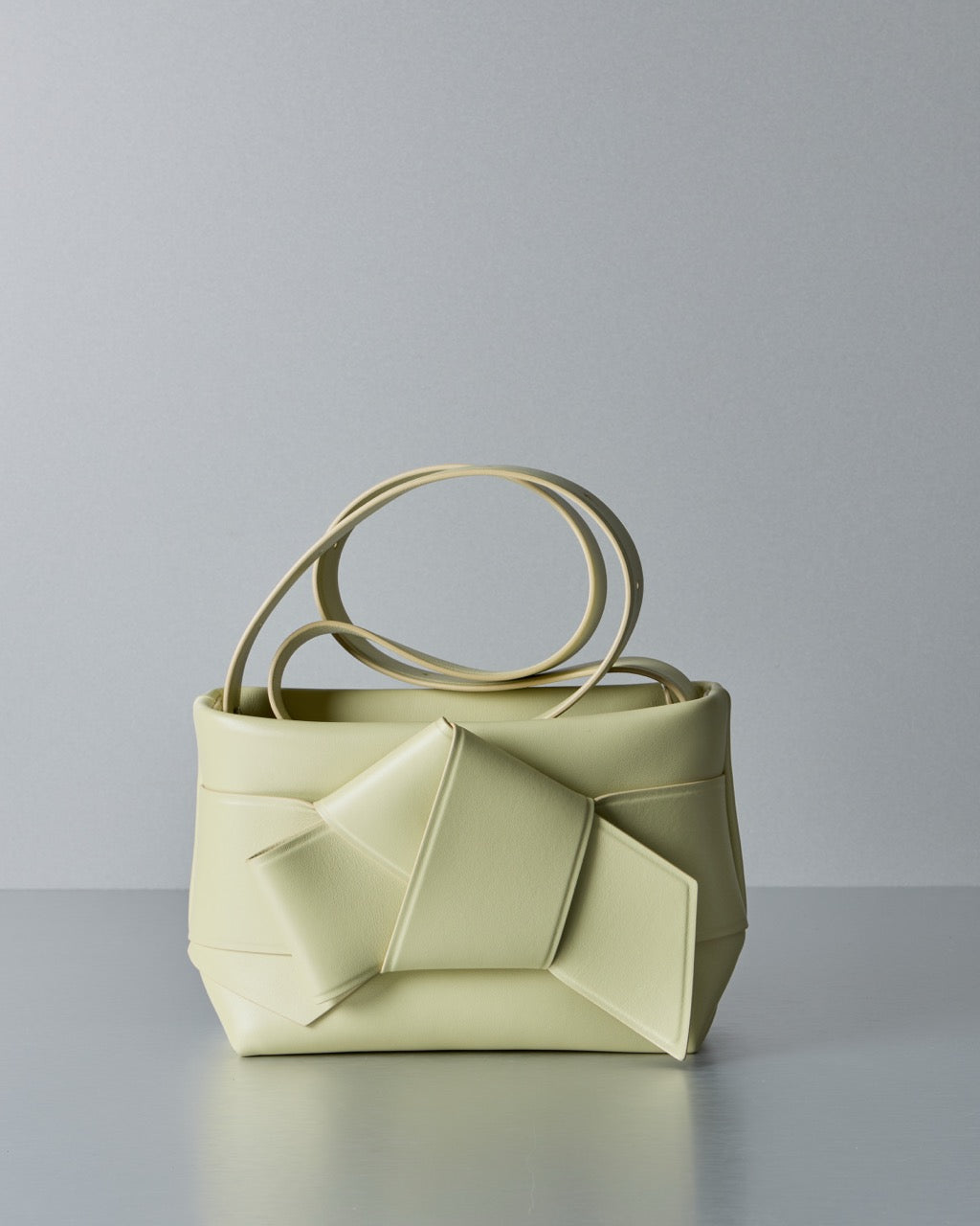 Light yellow Acne Studios handbag with unique circular handles on a gray background