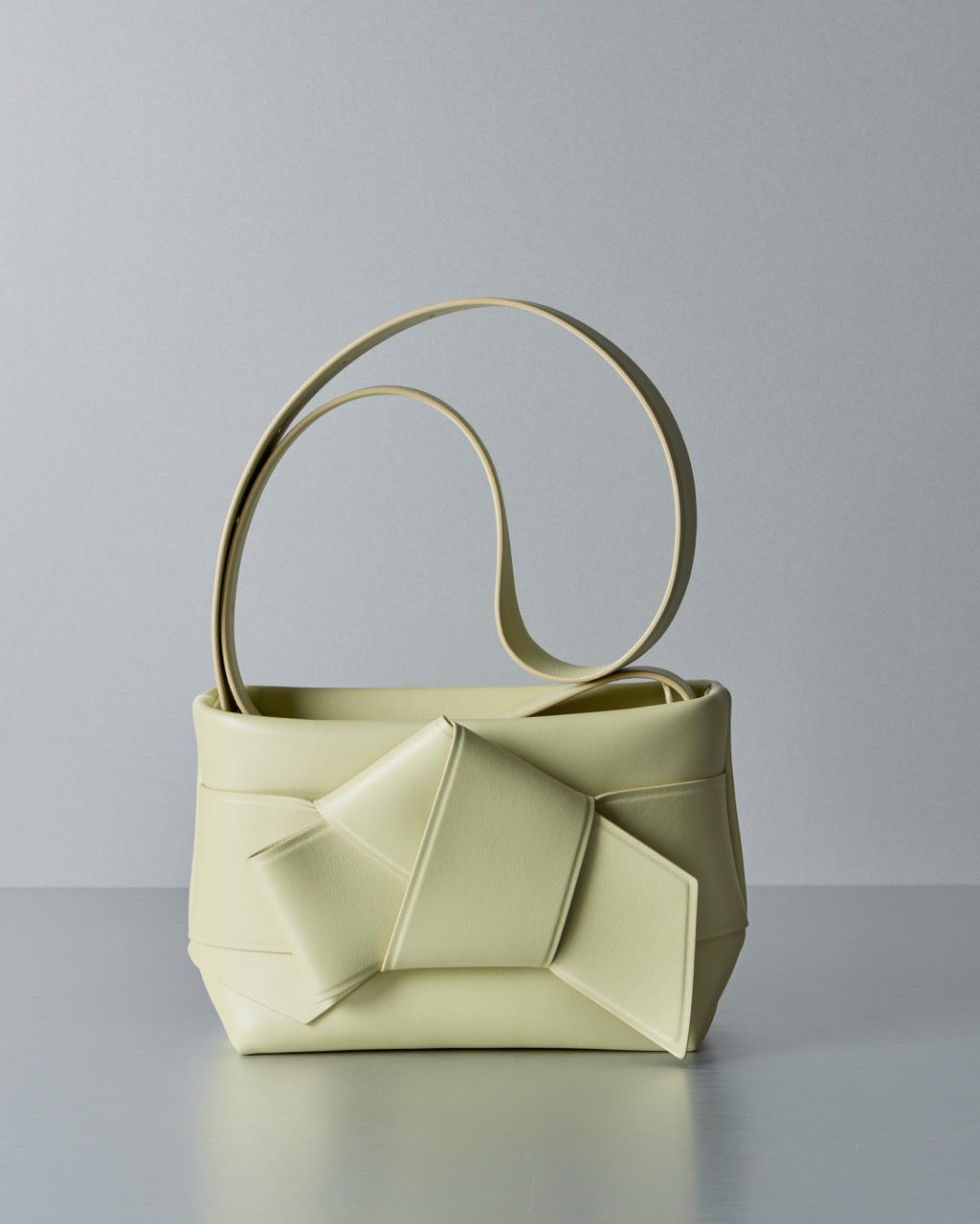 Light yellow Acne Studios handbag with unique circular handles on a gray background