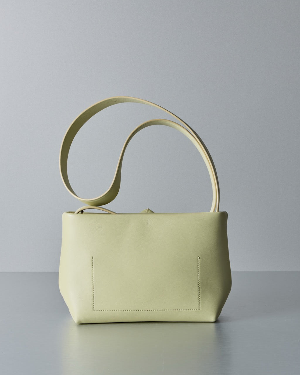 Light yellow Acne Studios handbag with a curved handle on a gray background.