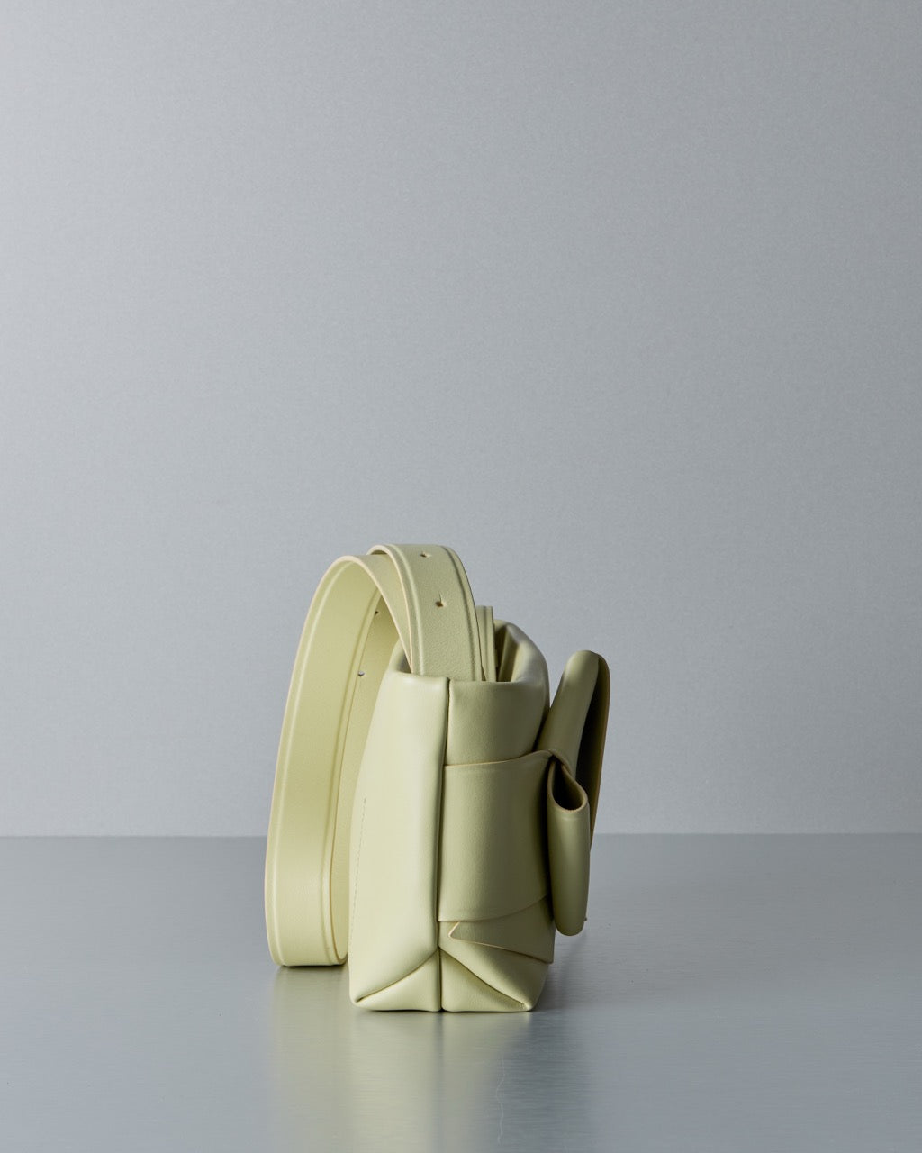 Light yellow Acne Studios leather handbag on a gray surface with a light gray background