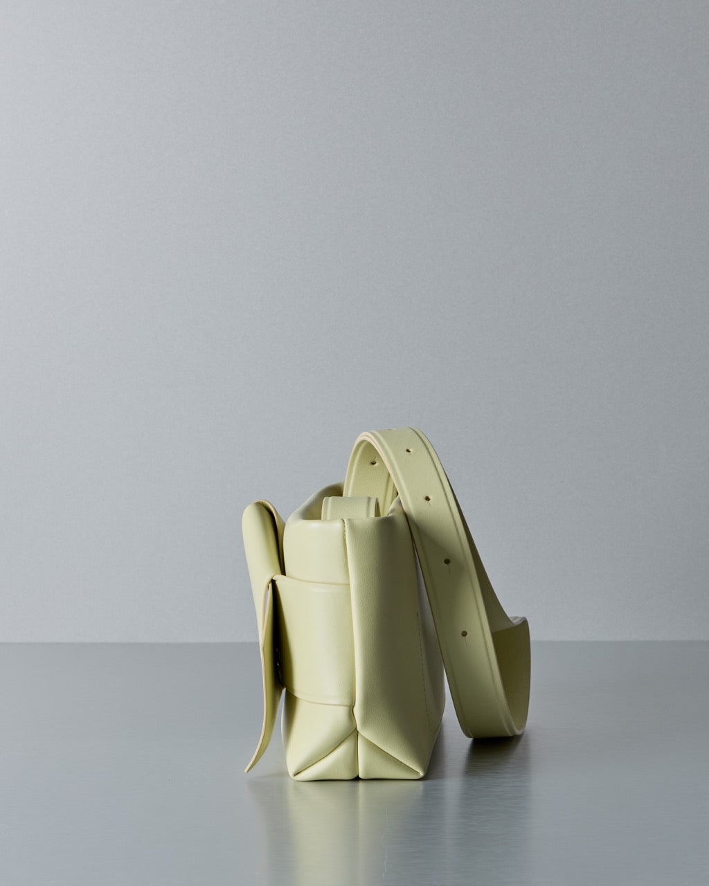 Light yellow Acne Studios handbag on a reflective surface with a gray background