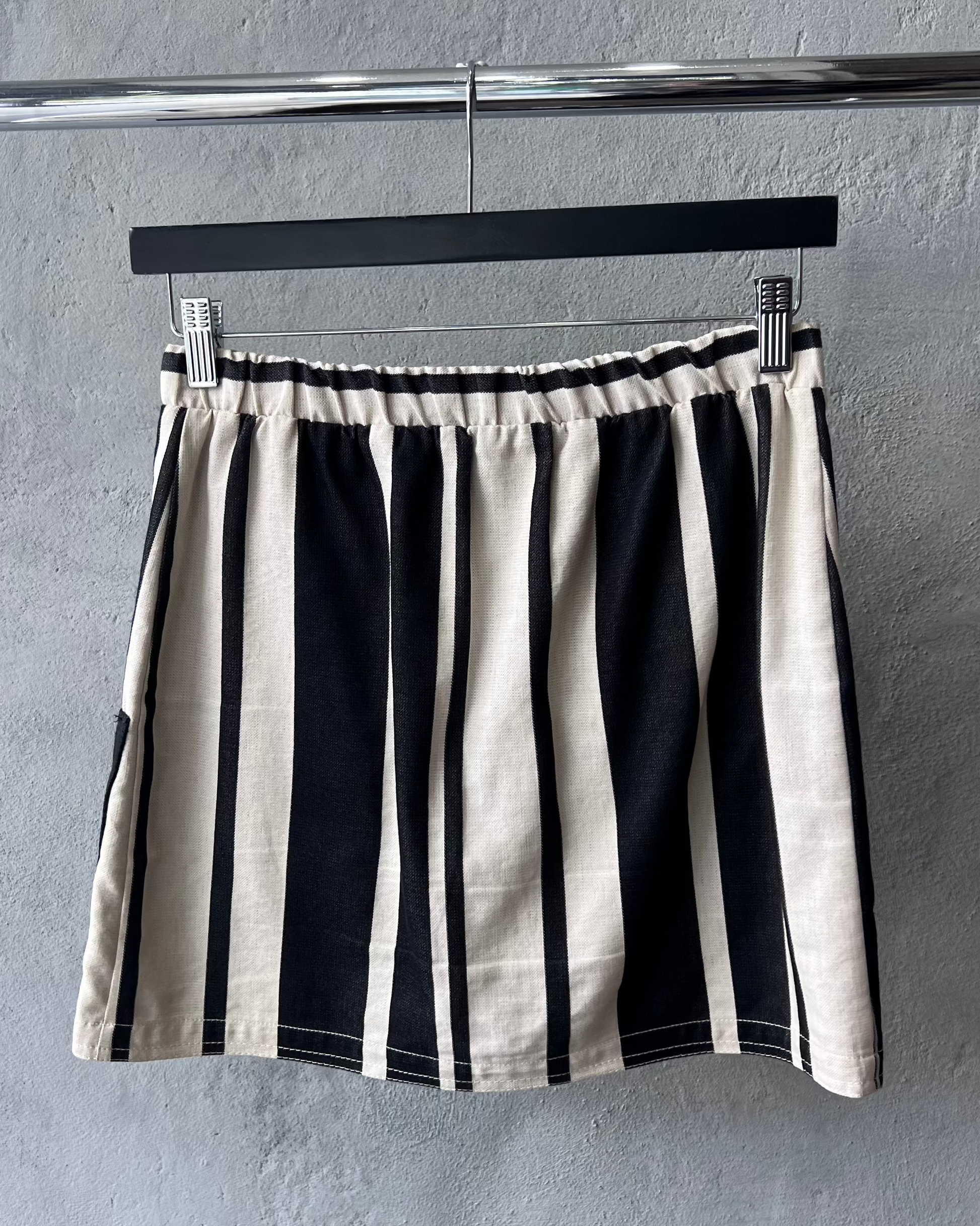 Black and white striped Acne Studios skirt hanging on a rack against a gray wall.