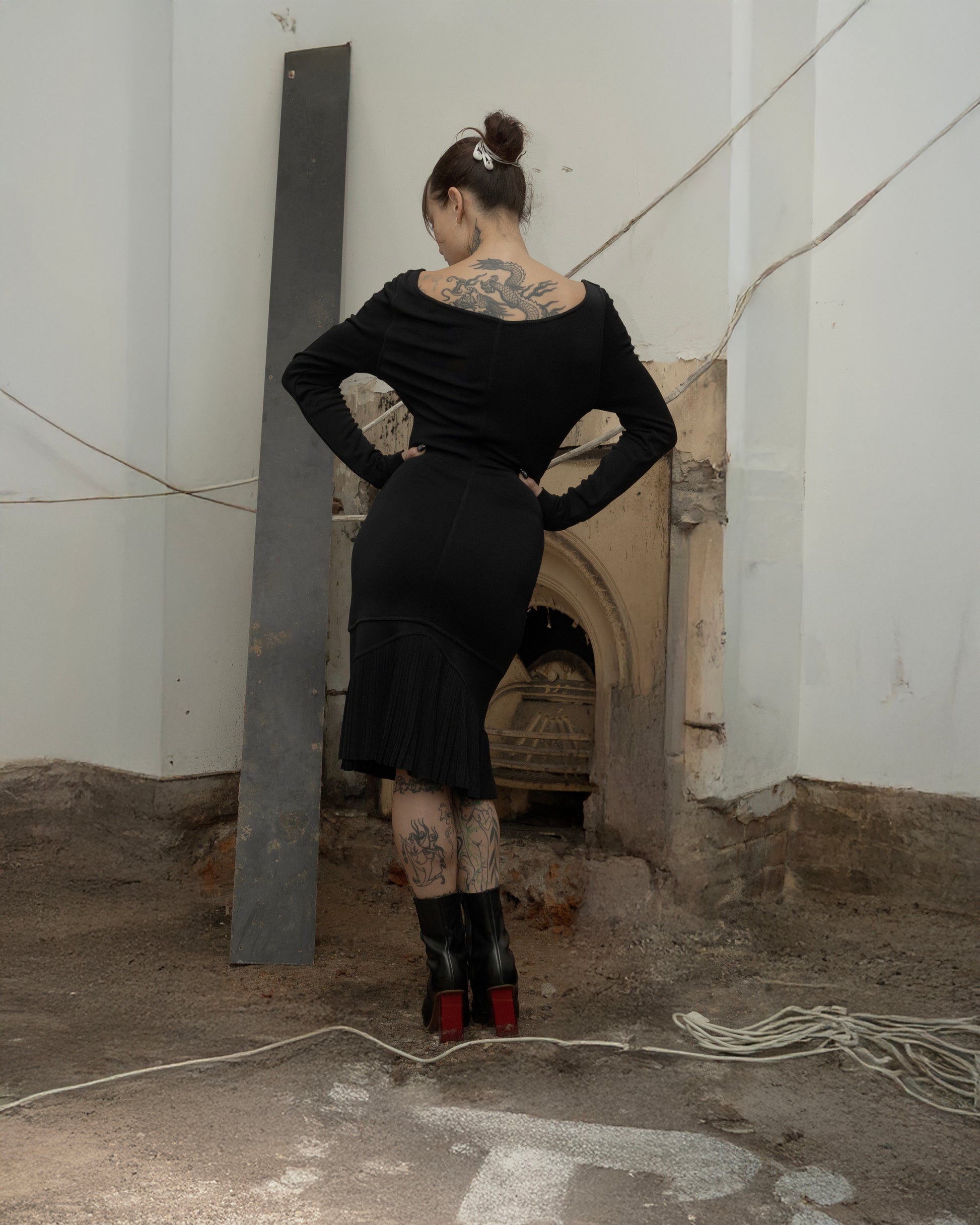 Person wearing a black Alaia outfit with tattoos standing in an industrial setting