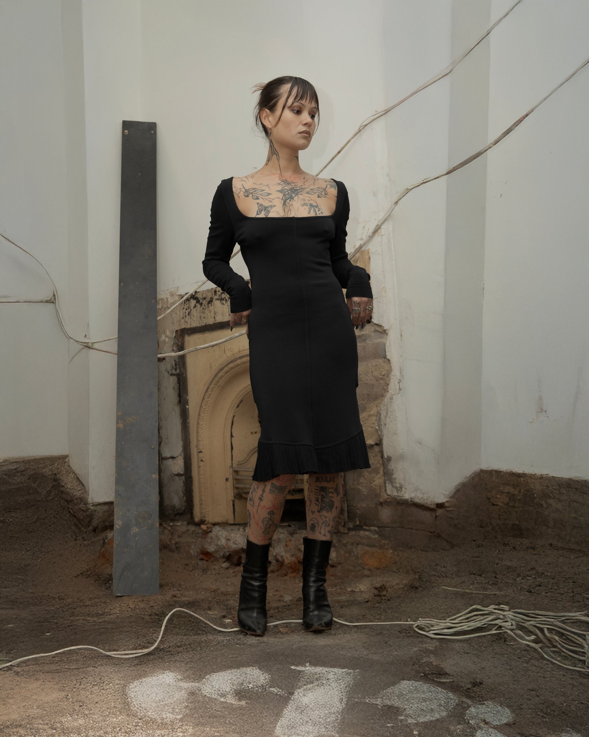 Person wearing a black Alaia dress with tattoos in an industrial setting