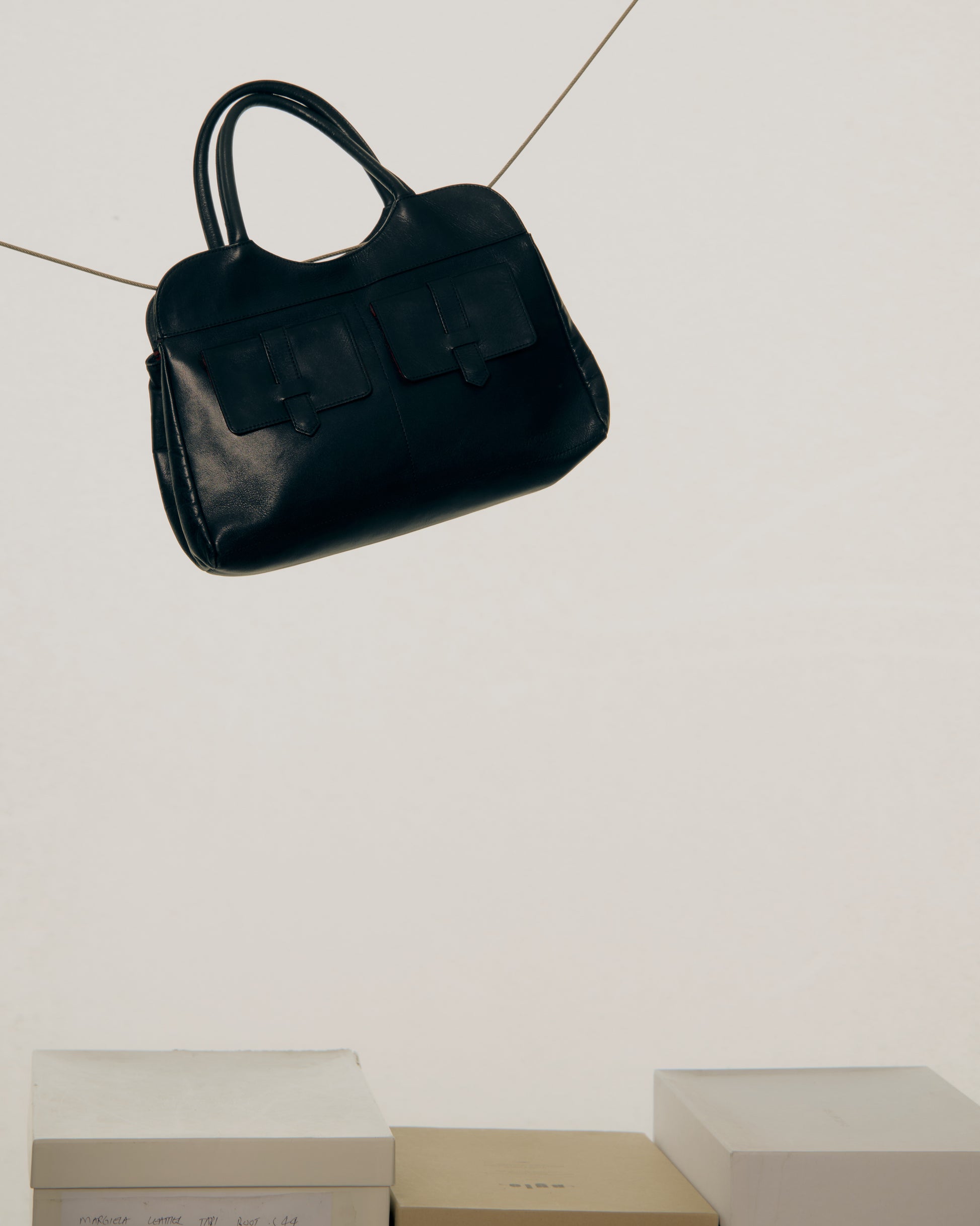 Black Alexander McQueen handbag hanging on a tiled wall with boxes below.