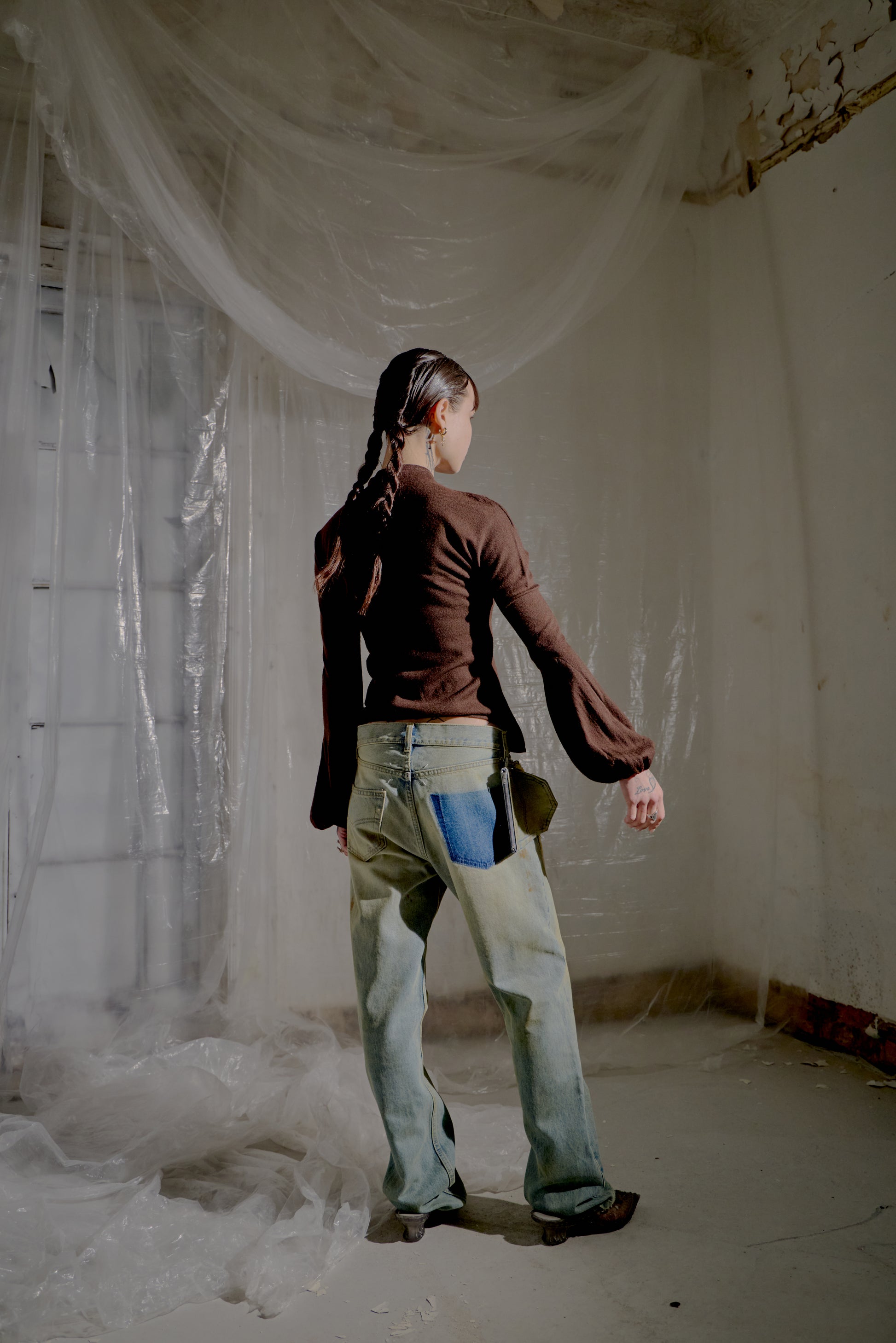Person standing in a room with white plastic sheeting on the walls and floor and wearing a brown Alexander McQueen blouse