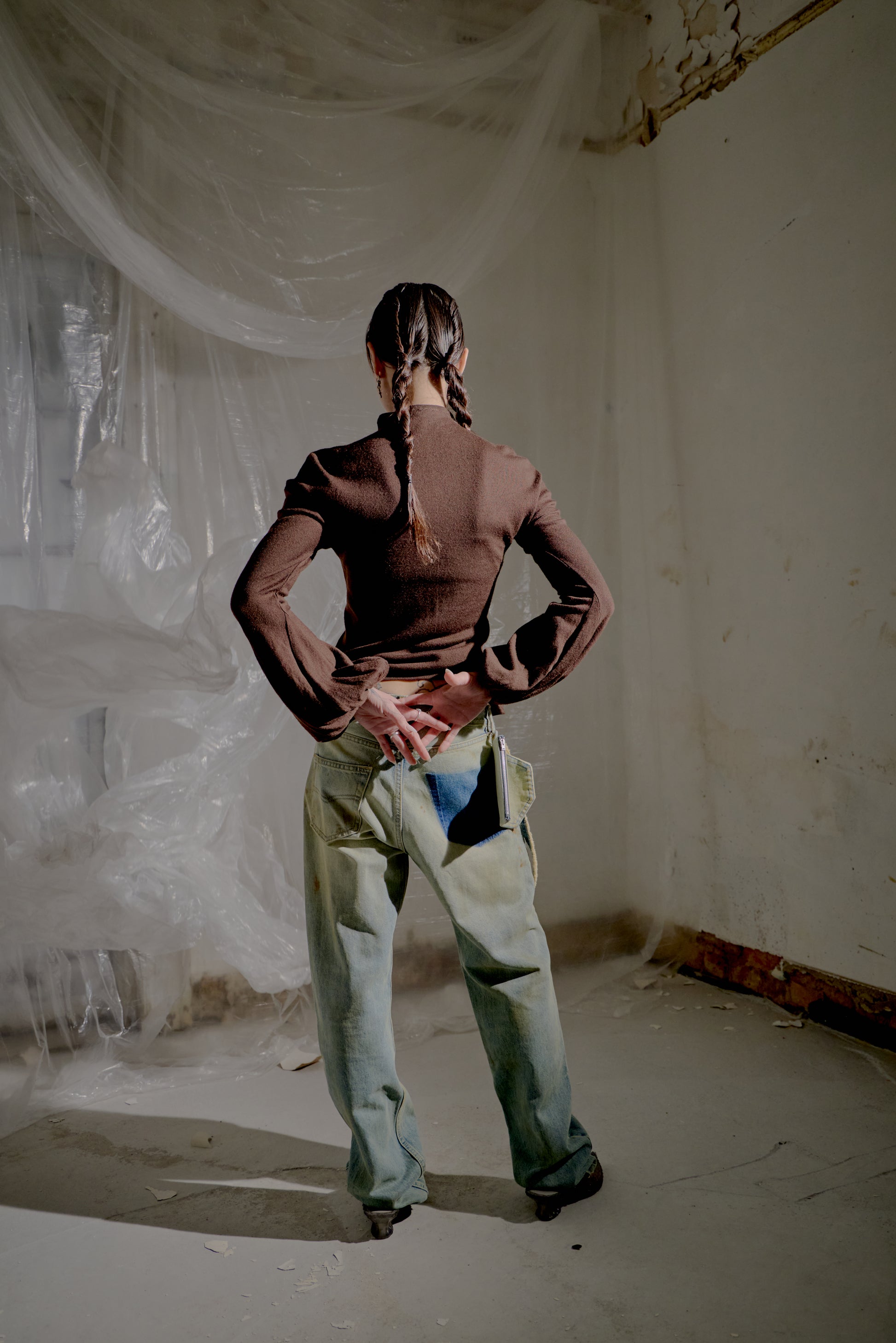 Person standing in a room with white plastic sheeting on the walls and floor and wearing a brown Alexander McQueen blouse