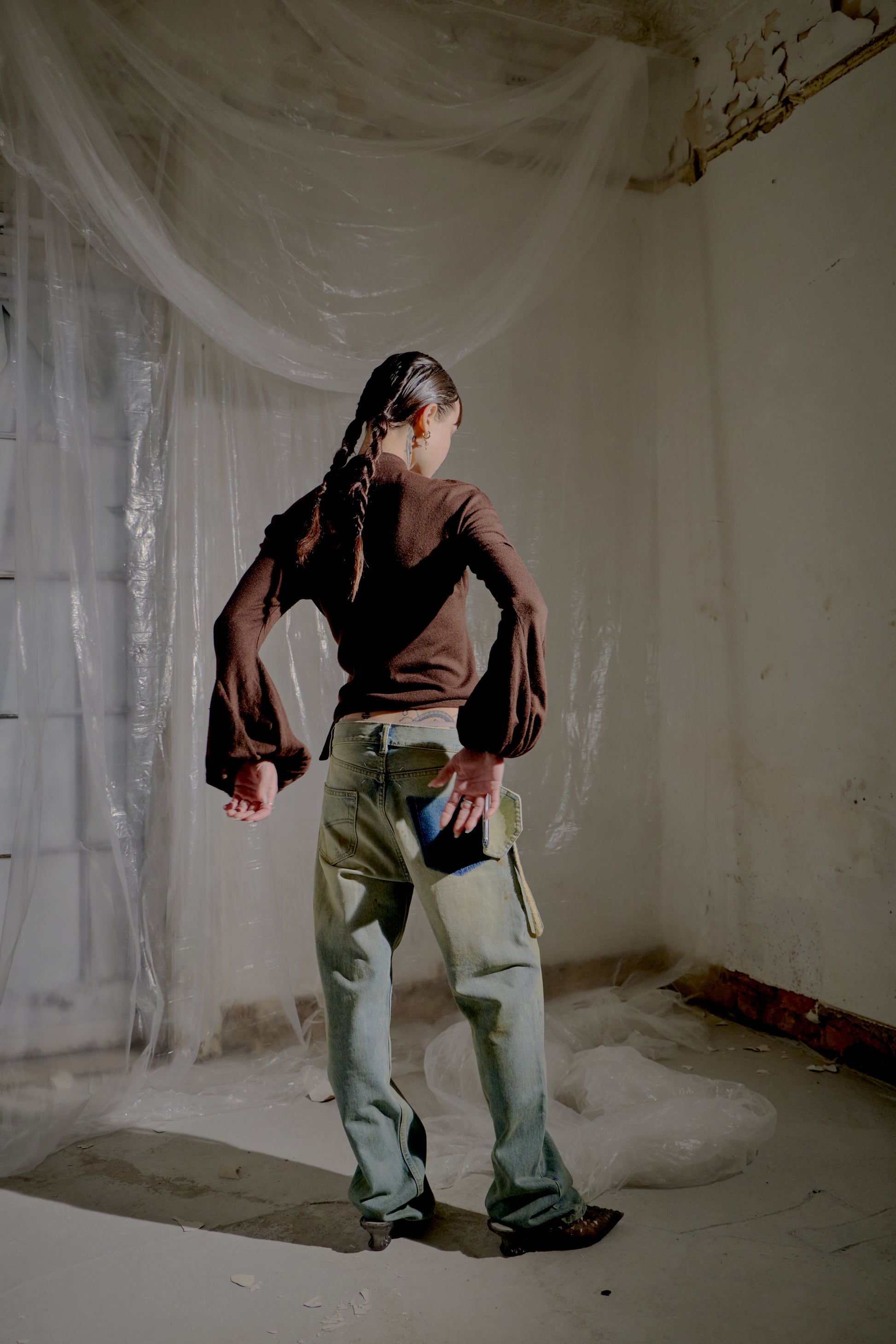 Person standing in a room with white plastic sheeting on the walls and floor and wearing a brown Alexander McQueen blouse