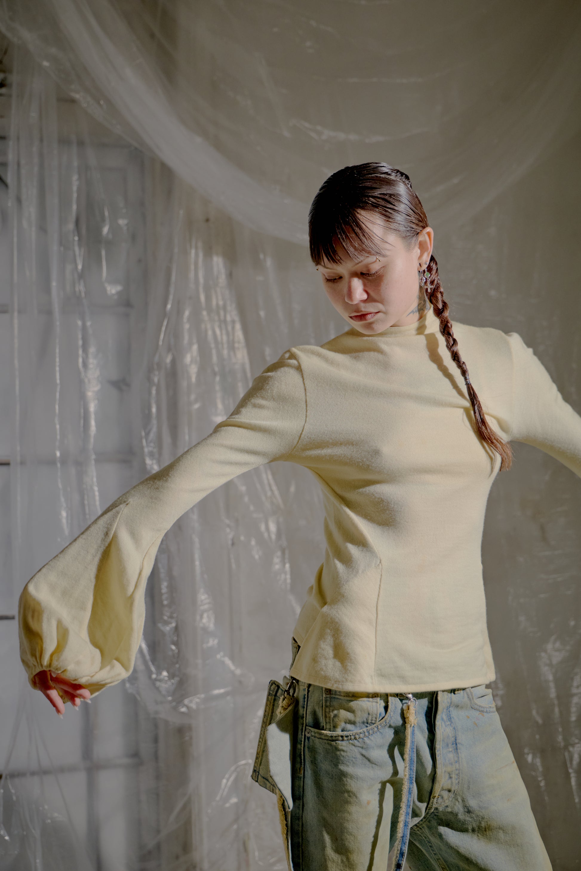 Person wearing a light-coloured long-sleeve Alexander McQueen top and jeans with a plain background