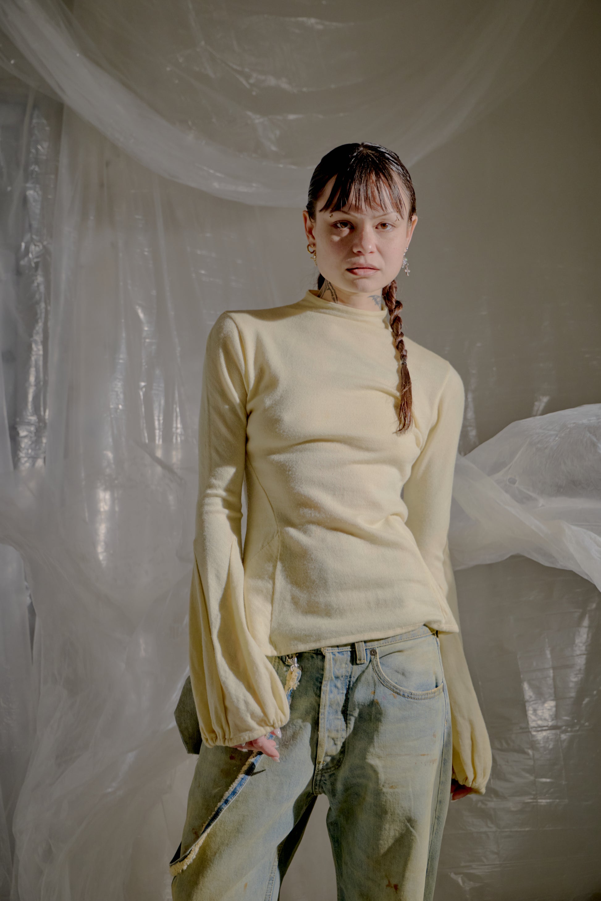 Person wearing a light yellow Alexander McQueen sweater and jeans standing against a plain background