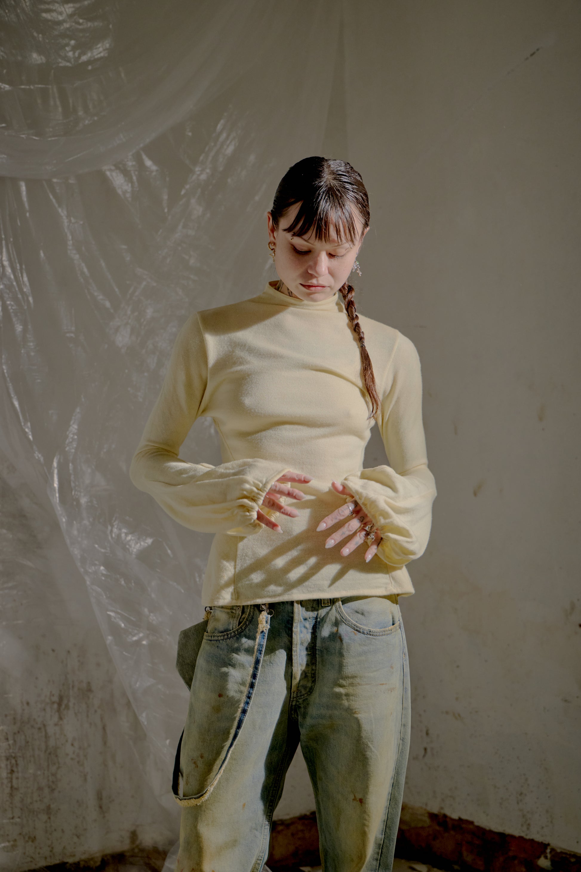 Person wearing a yellow long-sleeve Alexander McQueen top and light blue jeans against a plain wall.