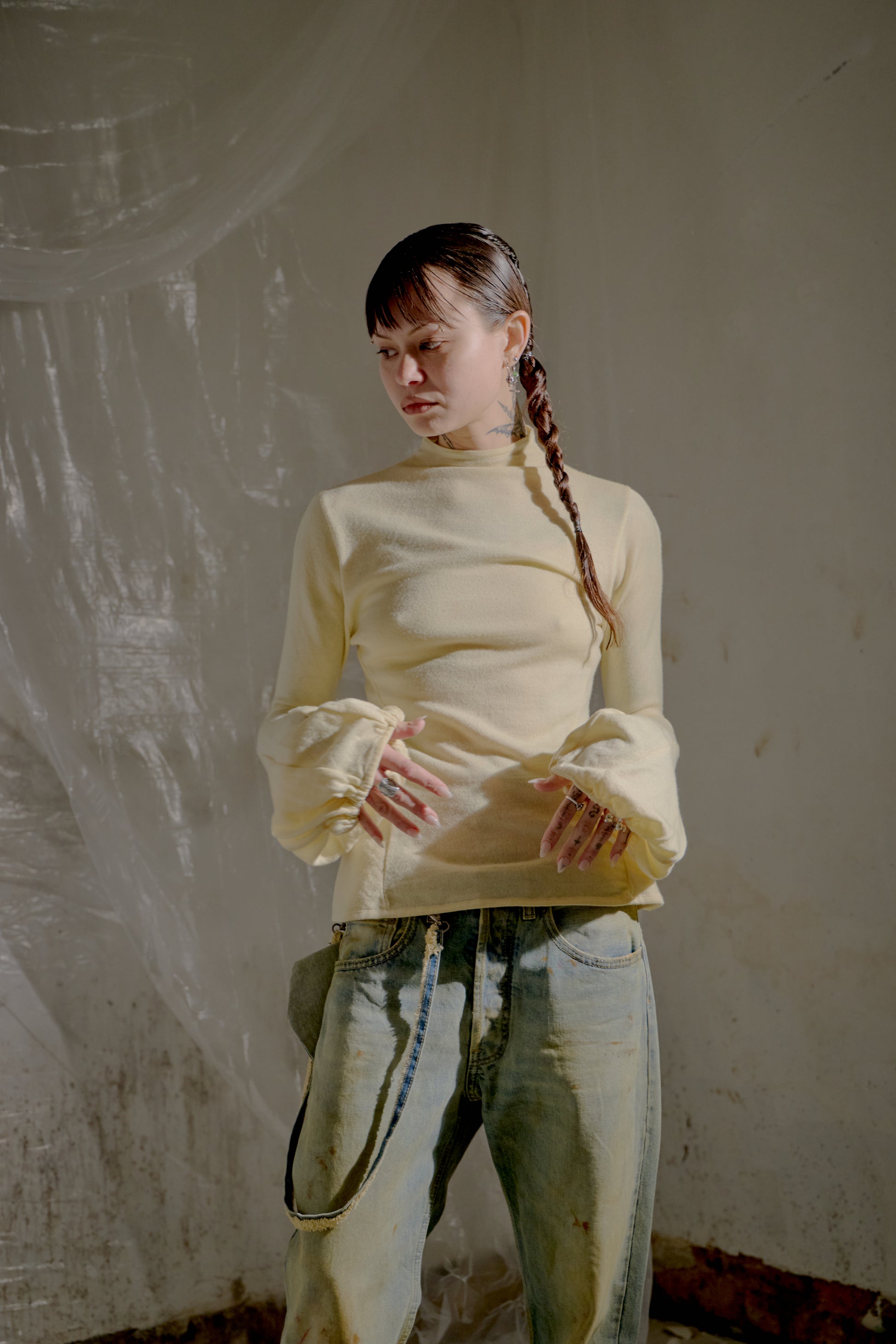 Person wearing a light yellow Alexander McQueen sweater and jeans against a textured wall.