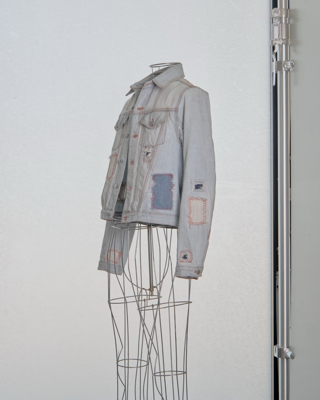 Denim Alexander McQueen jacket with patches on a mannequin against a light gray background