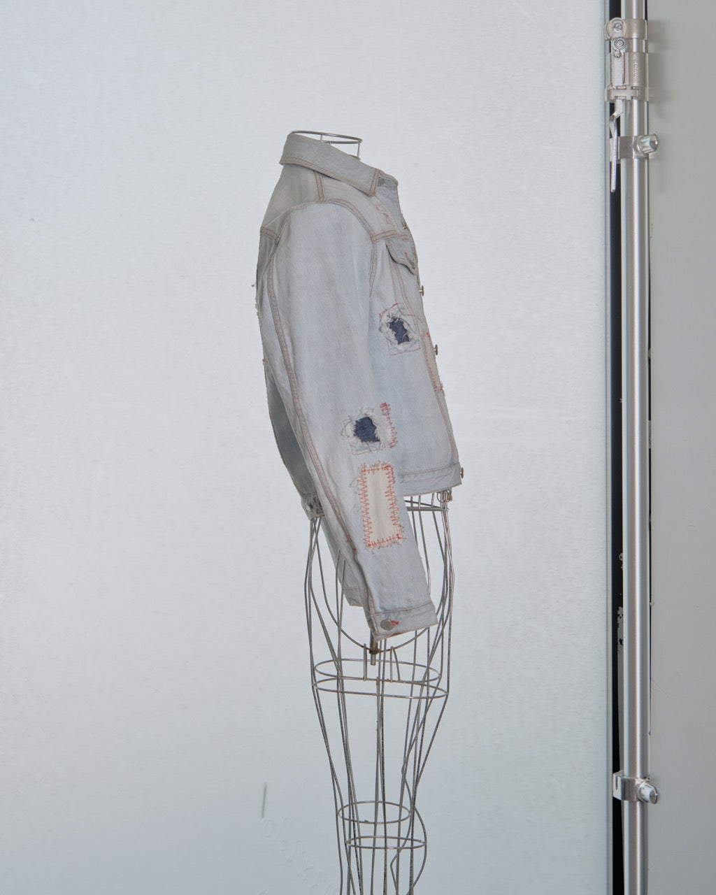 Denim Alexander Mcqueen jacket with patches on a wire mannequin against a white background