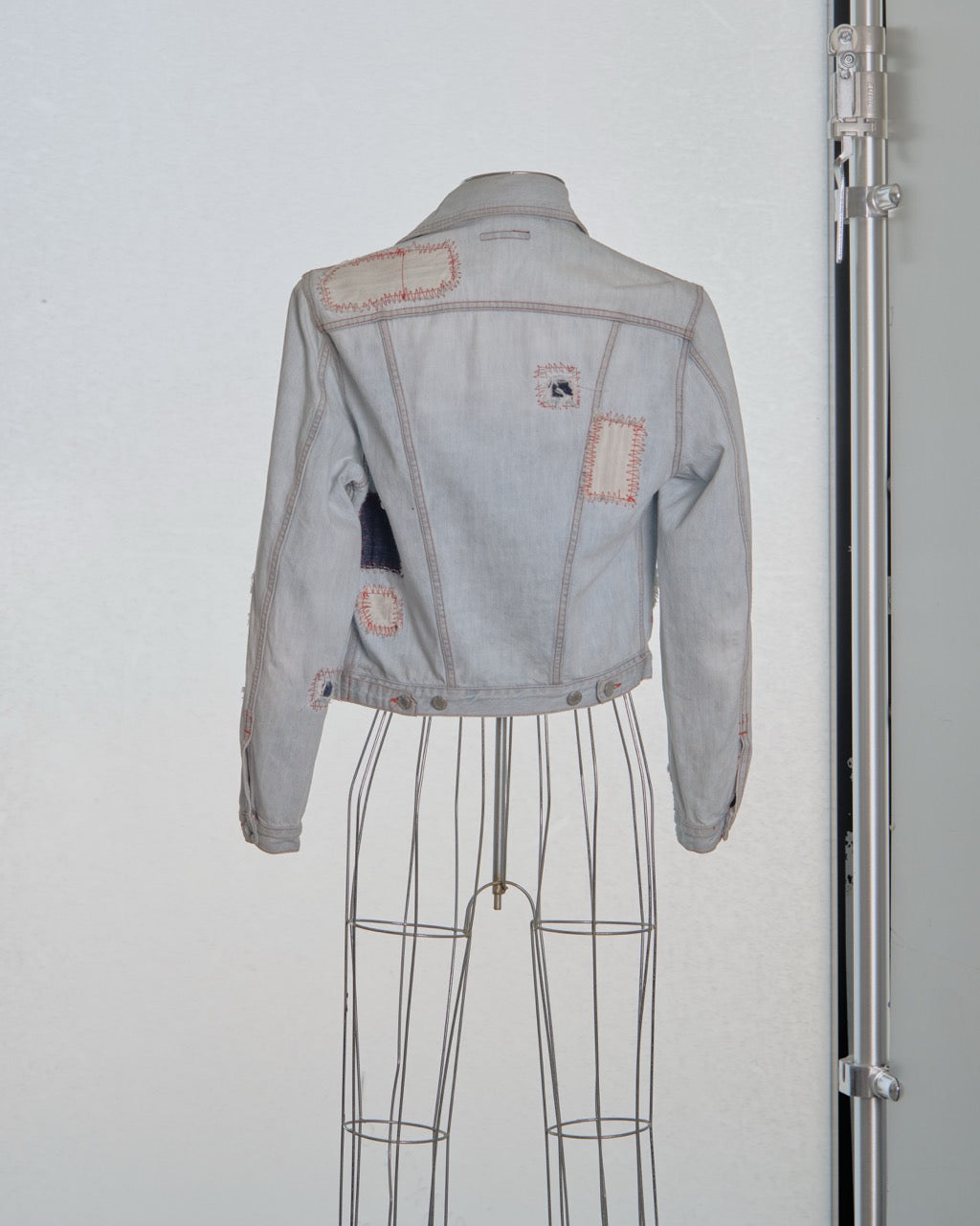 Denim Alexander McQueen jacket with patches on a mannequin against a white background