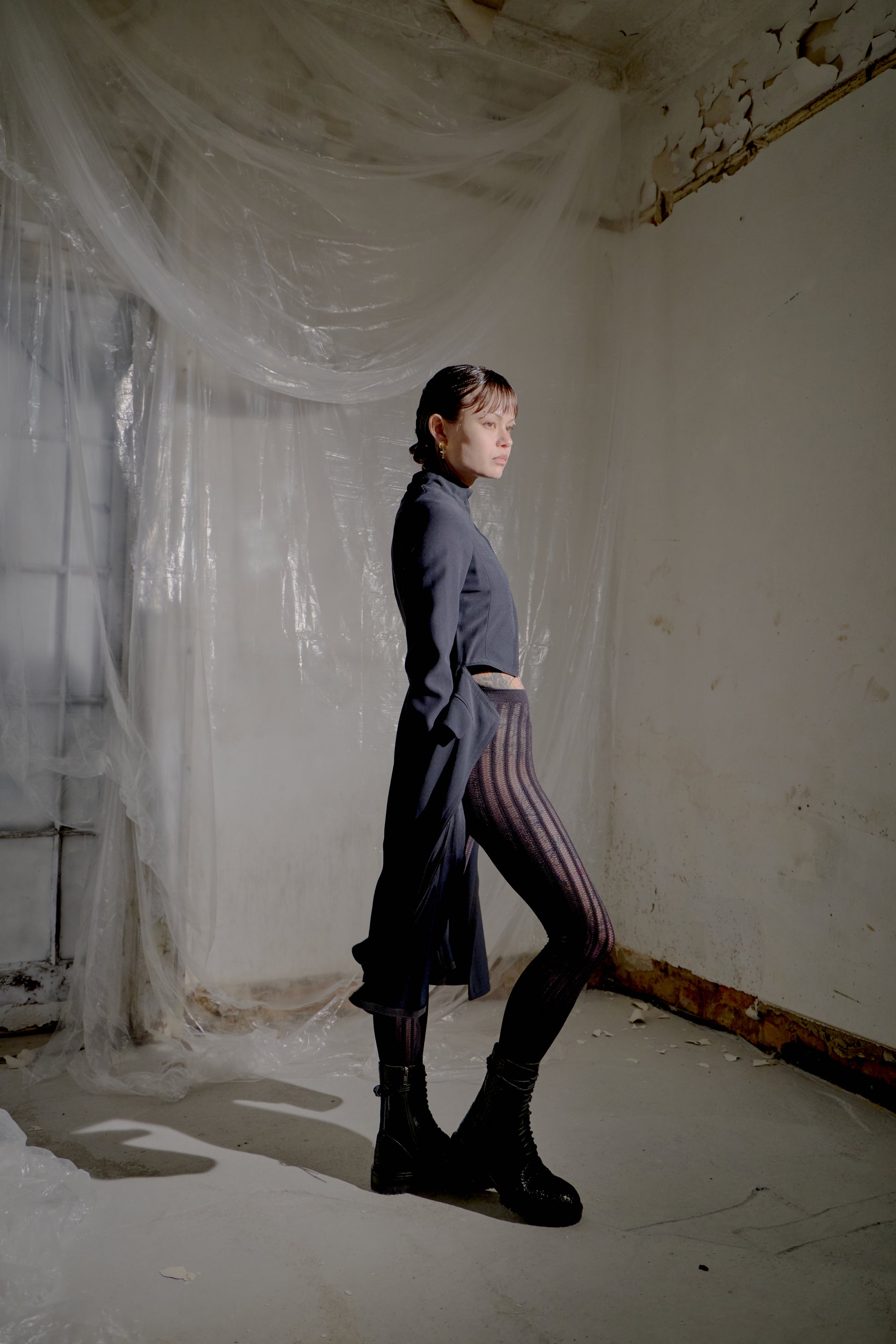 Person standing in a room with white walls and a window covered by plastic sheeting.
