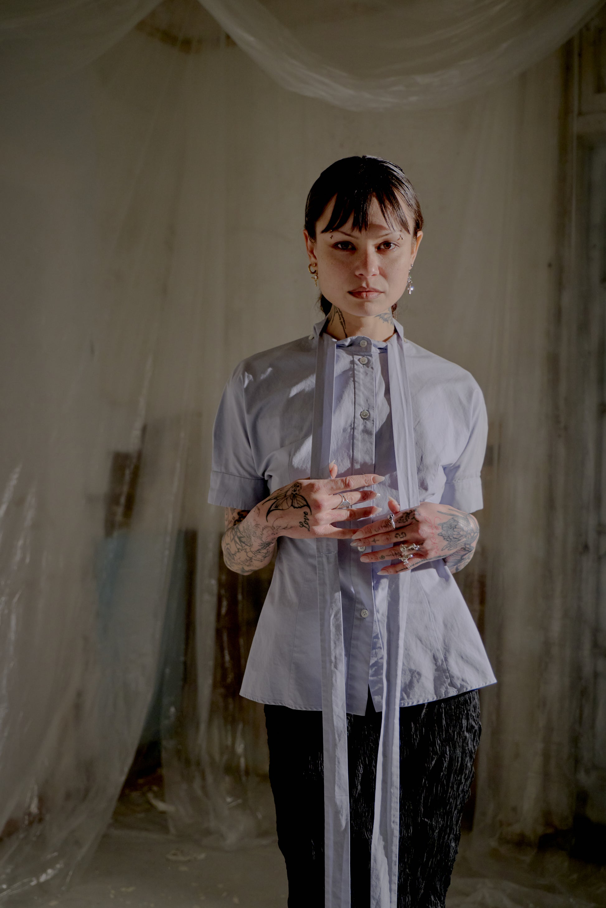 Person wearing a light-colored Alexander McQueen shirt with sheer sleeves in a softly lit room.