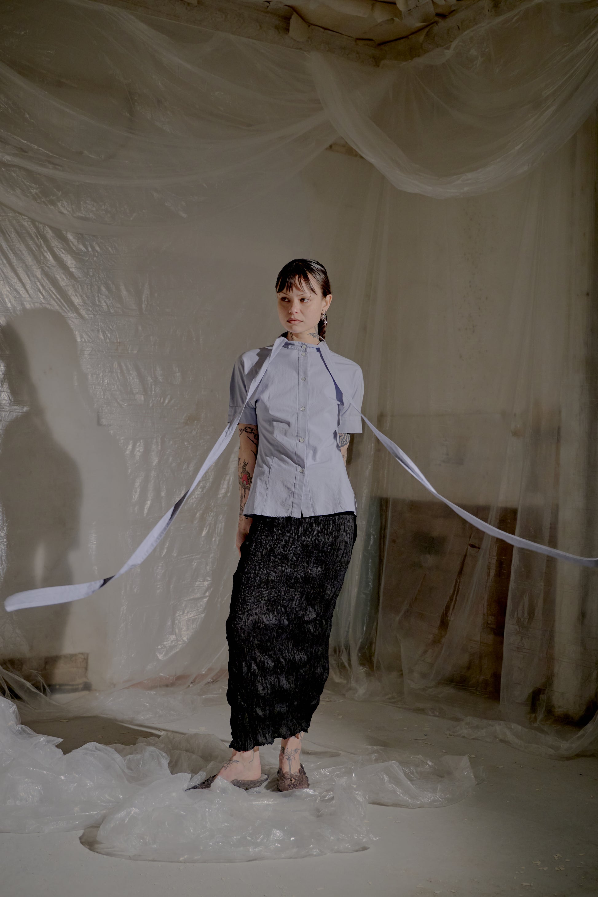 Person standing in a room with draped fabric and wearing an Alexander McQueen shirt