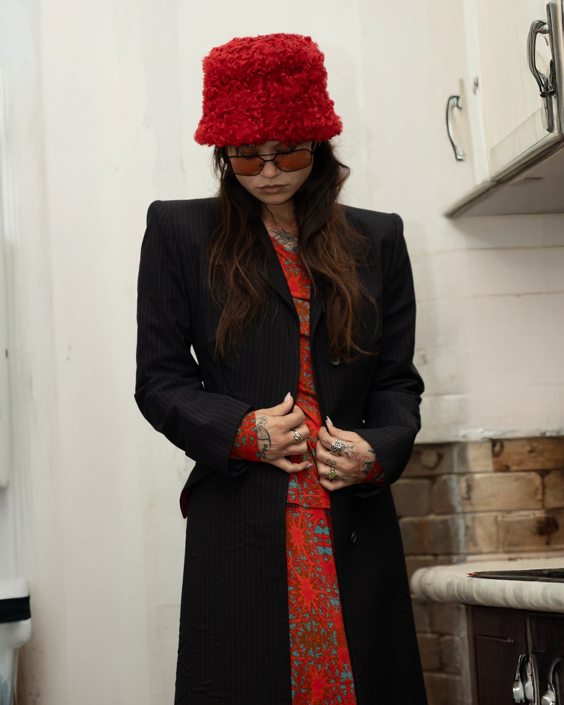 Person wearing a red knitted hat and black  Alexander McQueen coat in a kitchen setting.