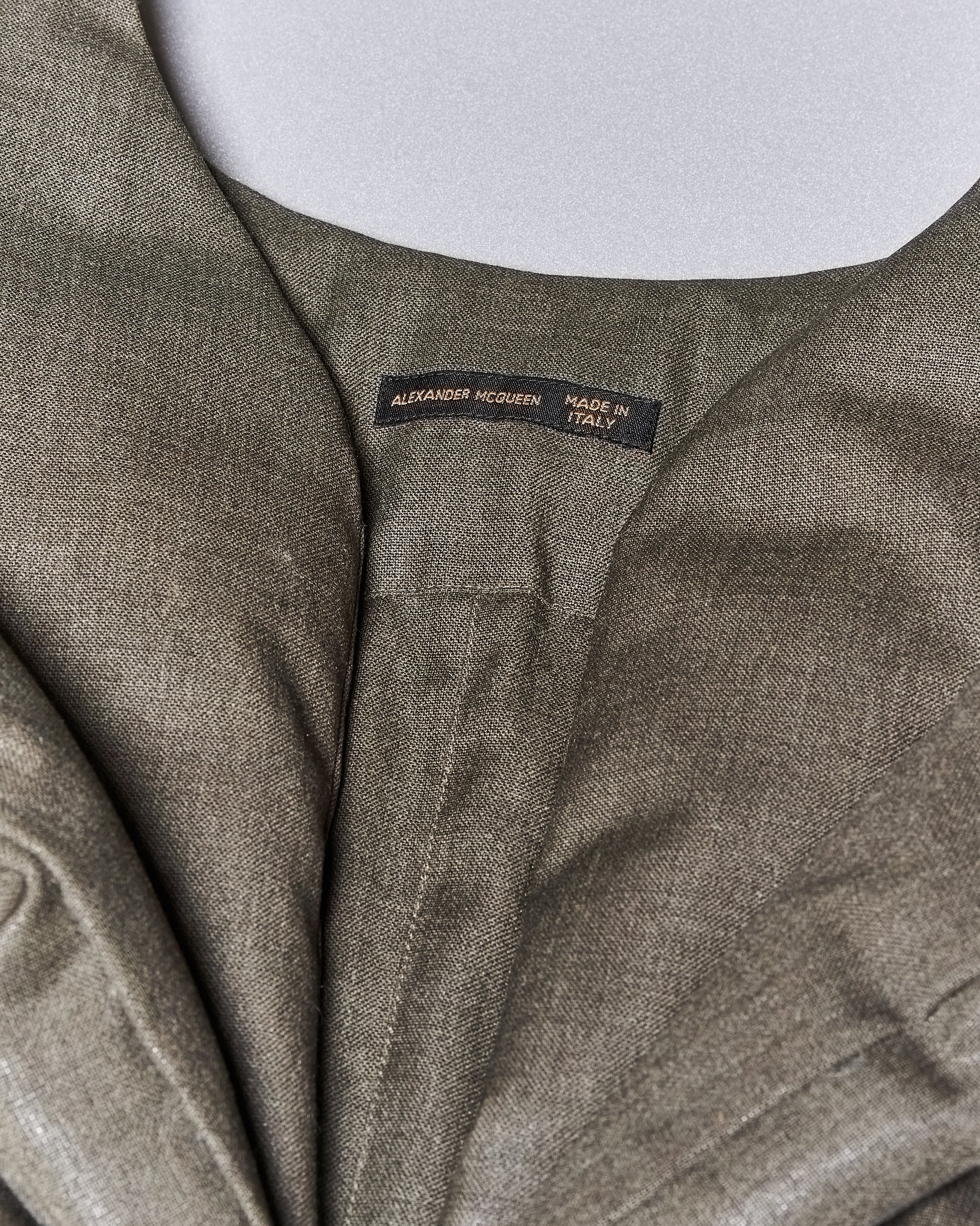 Close-up image of a grey-green garment with a label reading "Alexander McQueen Made in Italy." The fabric appears textured and luxurious.