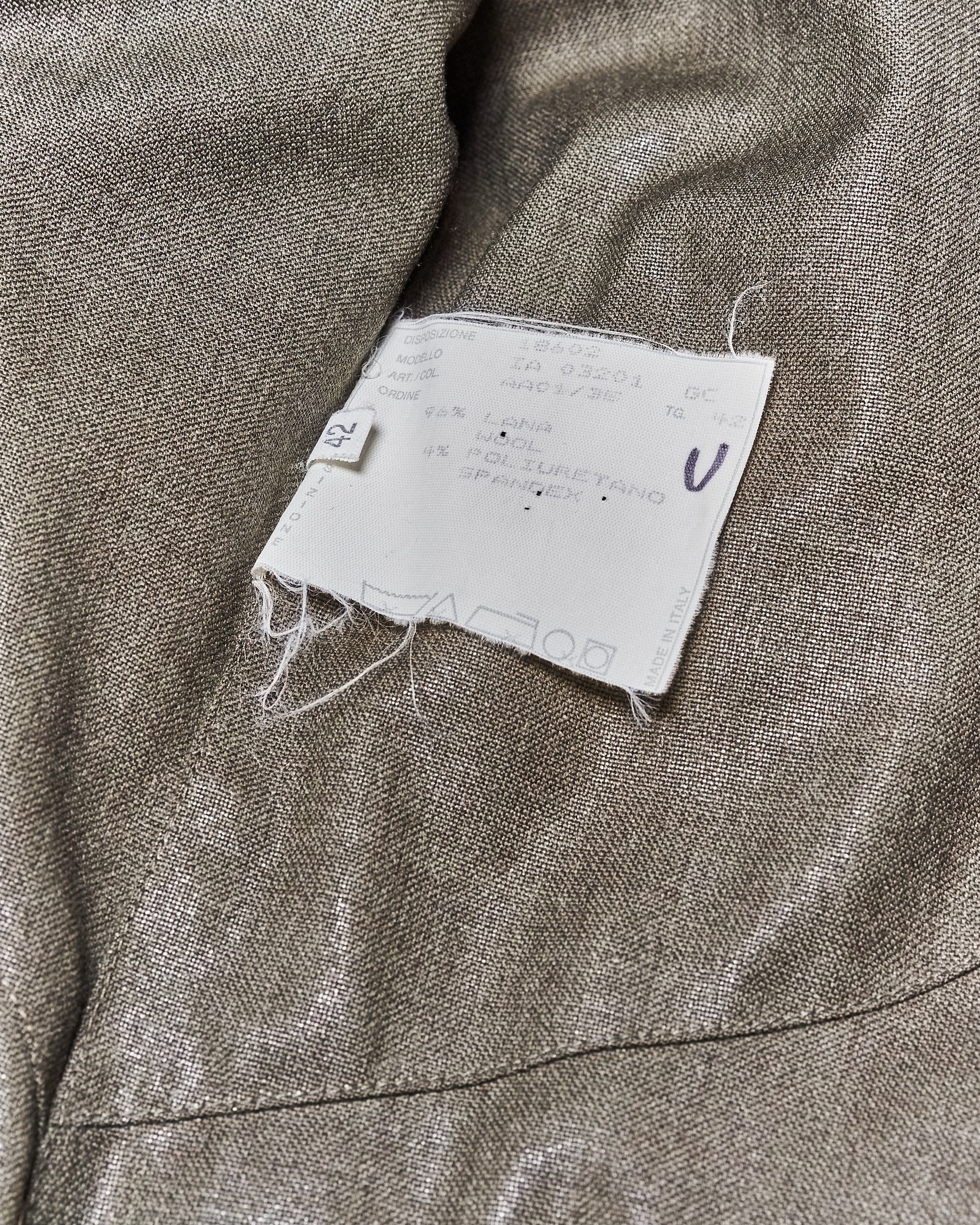 Close-up of an Alexander McQueen clothing tag on a green fabric. The tag displays care instructions and fibre content including wool and spandex in multiple languages. Frayed edges suggest wear.