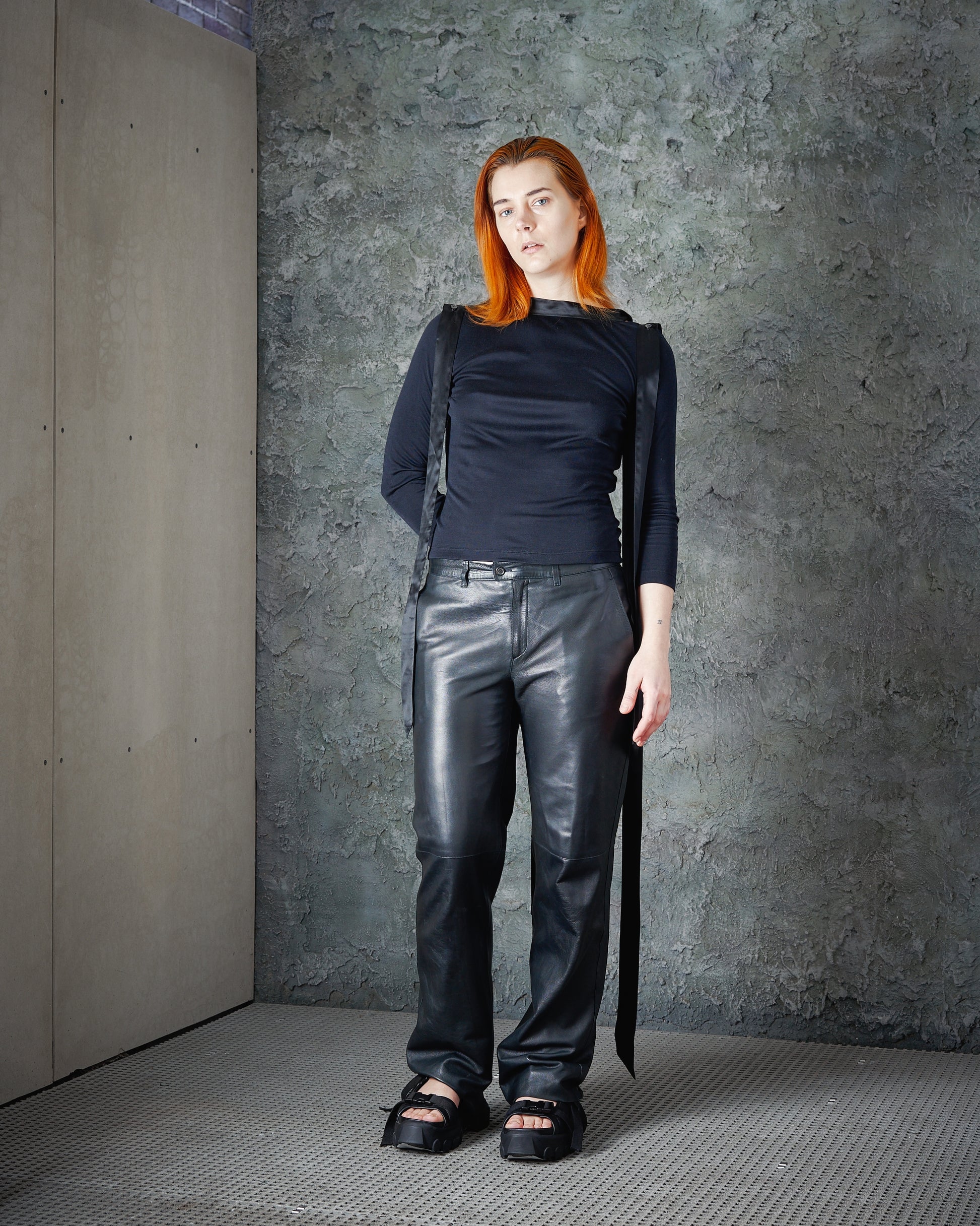 A model wearing a high-neck Alexander McQueen top with silk ribbon details on the collar and a draped open back, paired with trousers.