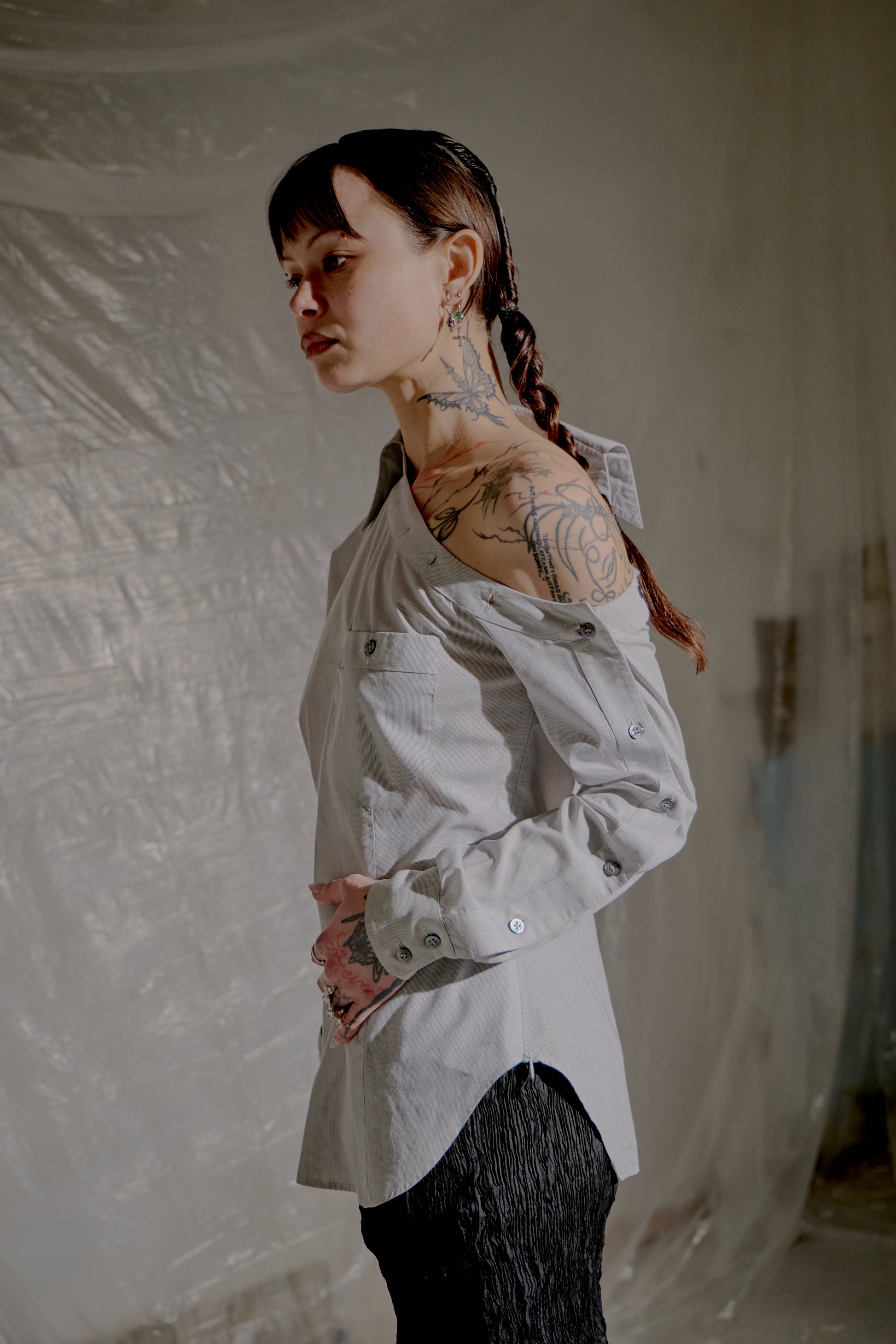 Person wearing a light-coloured Alexander McQueen shirt with tattoos visible on arms and neck, standing against a plain background.