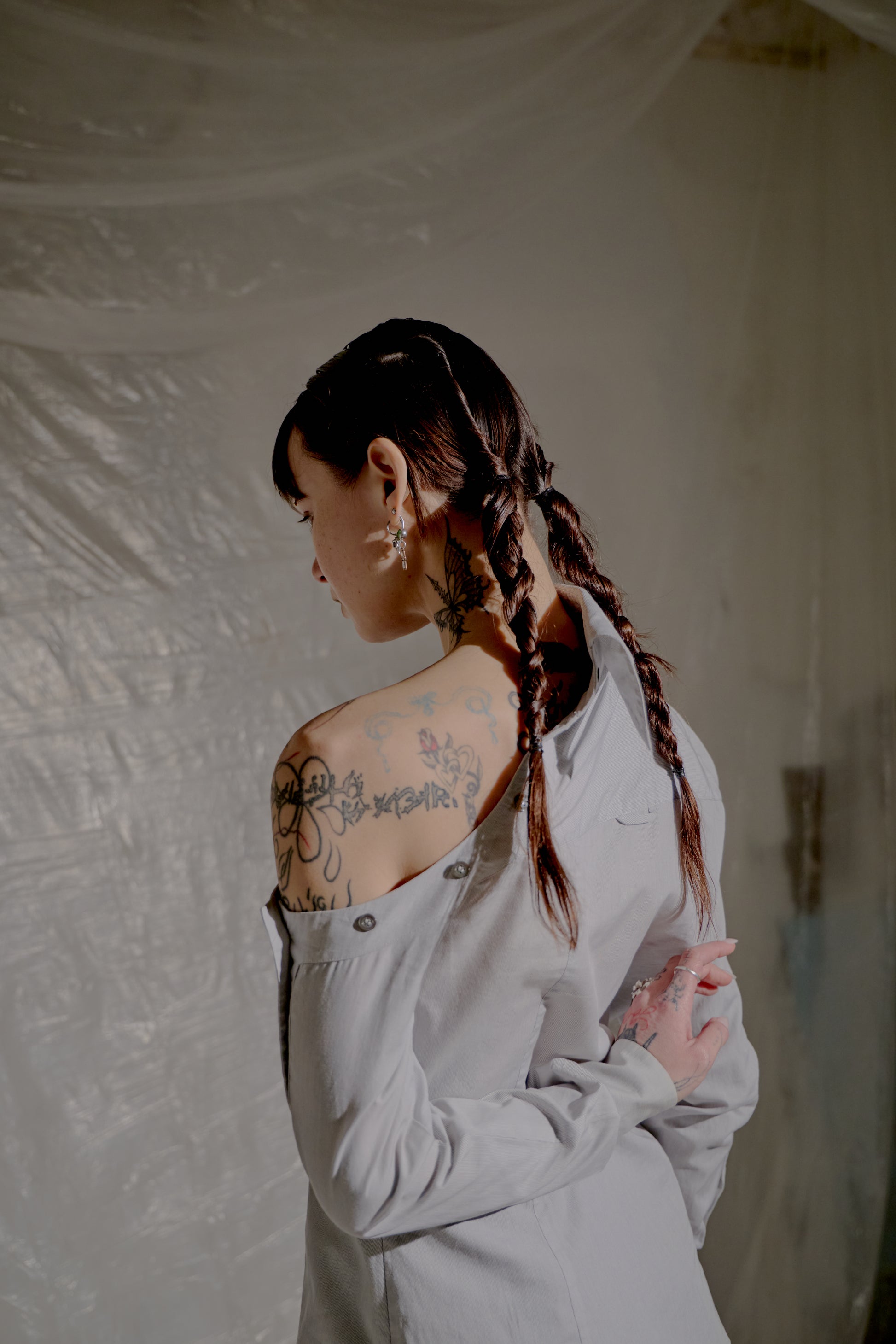 Person wearing a light grey Alexander McQueen shirt with braided hair against a plain background.