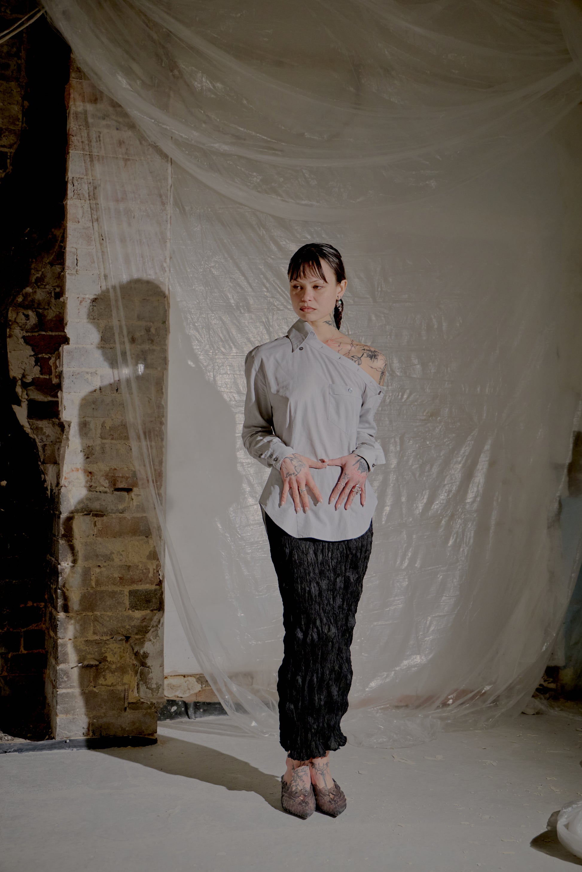 Person standing in a room with draped fabric and brick wall wearing an Alexander McQueen shirt