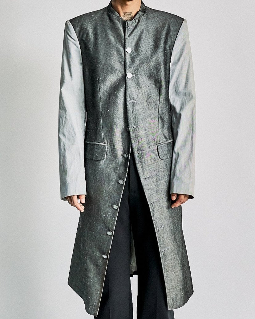 A model wearing a long, silver metallic Alexander McQueen coat with light grey sleeves and button details.