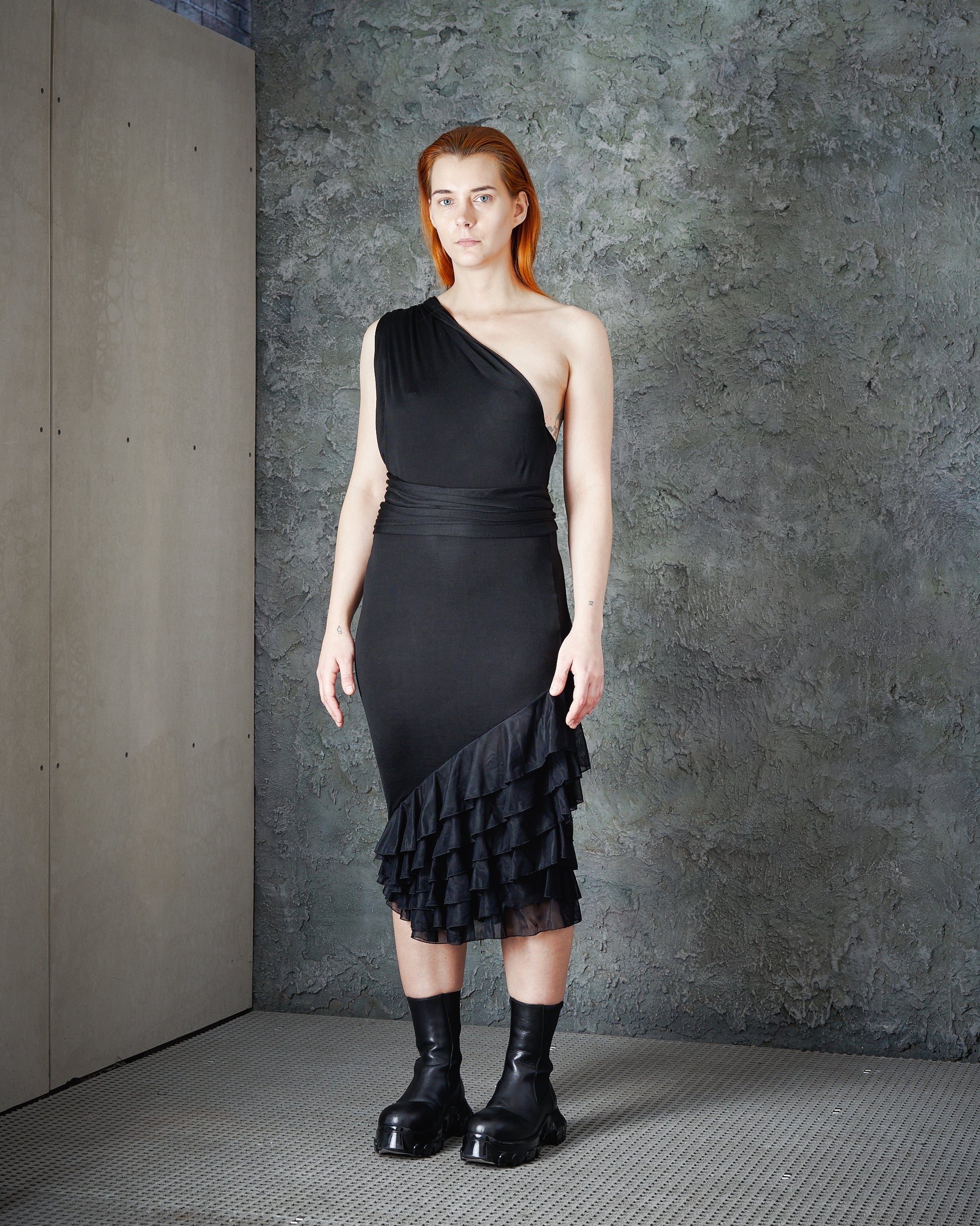 A model wearing a one-shoulder Alexander McQueen black dress with ruffle layers and a trailing fabric shoulder sash.
