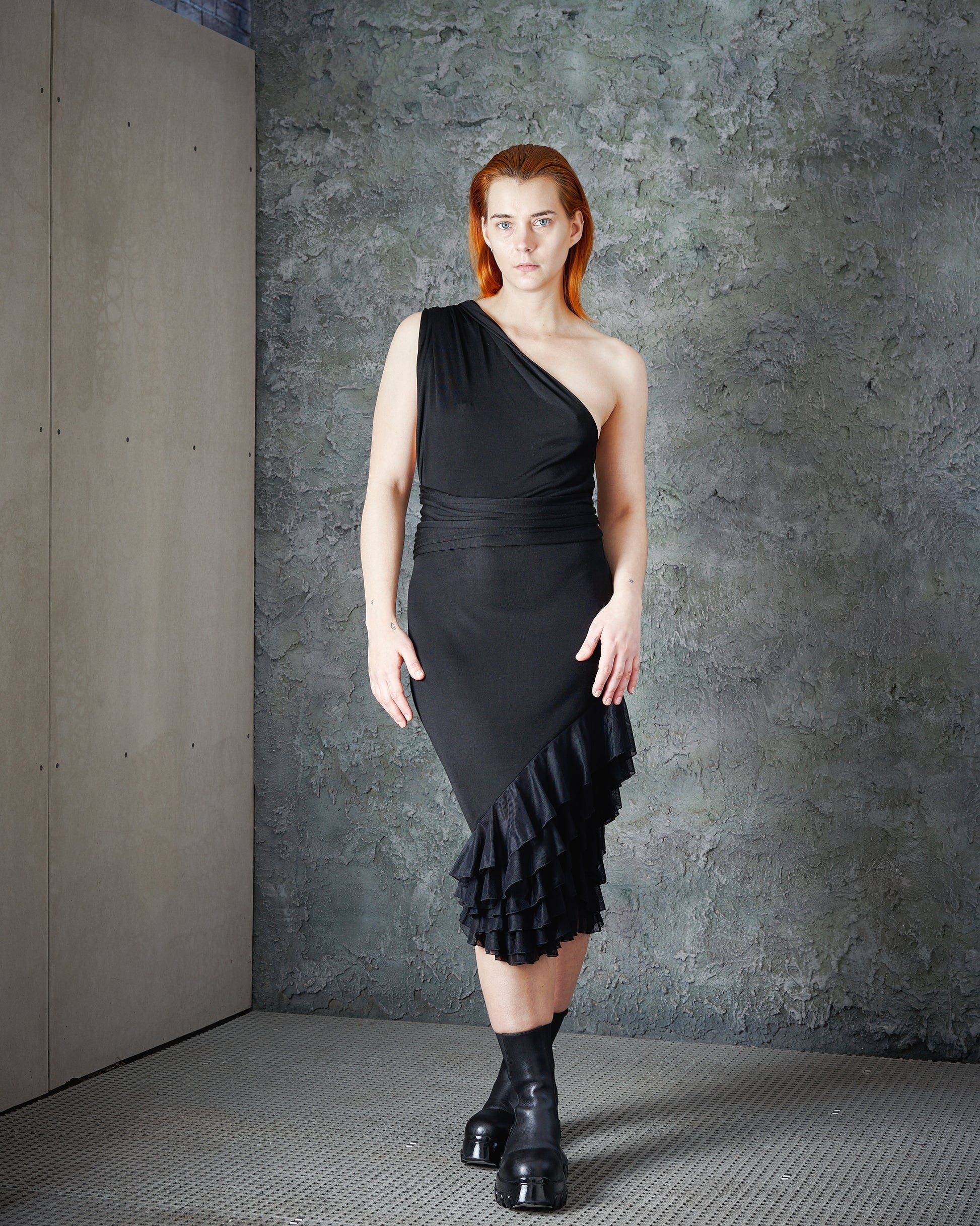 A model wearing a one-shoulder Alexander McQueen black dress with ruffle layers and a trailing fabric shoulder sash.