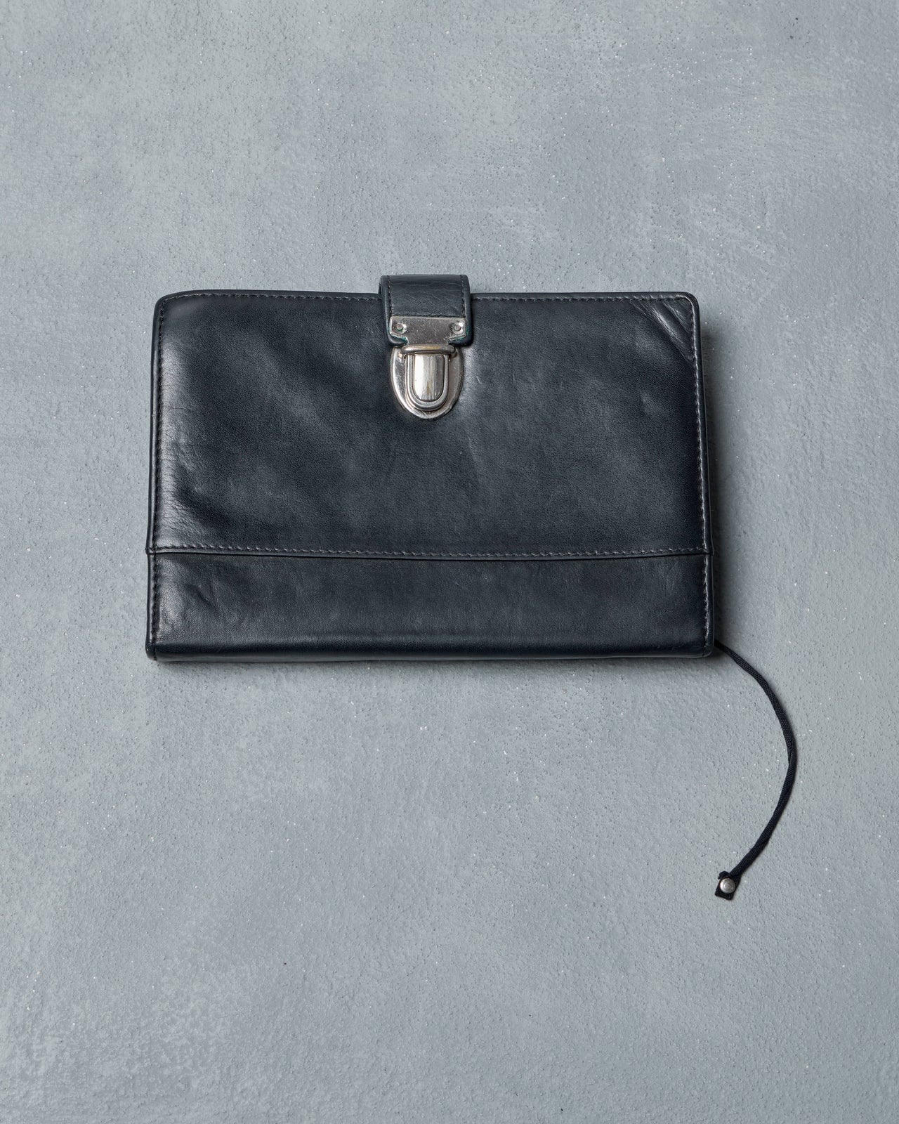 Black Ann Demeulemeester travel wallet with a silver clasp on a gray background