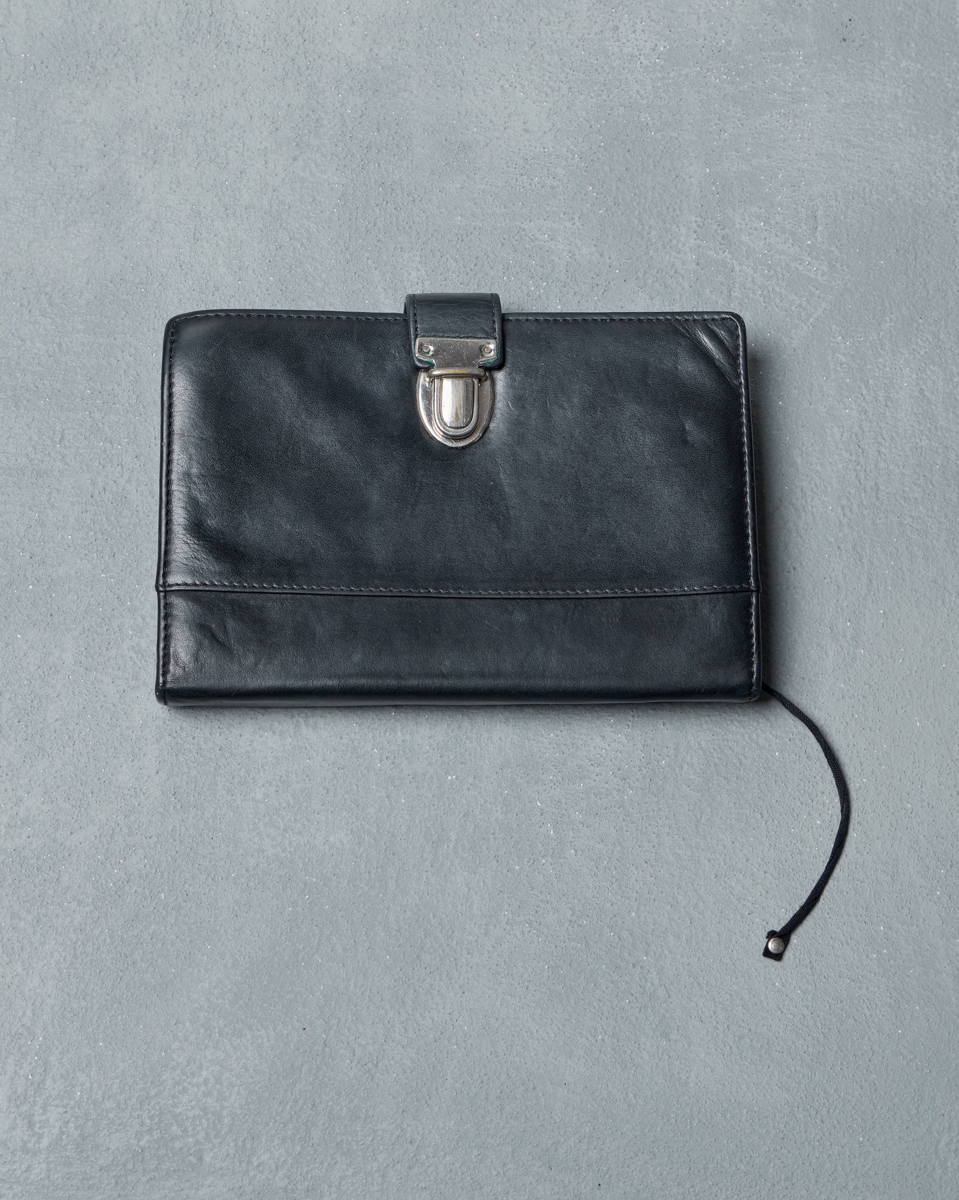 Black Ann Demeulemeester travel wallet with a silver clasp on a gray background