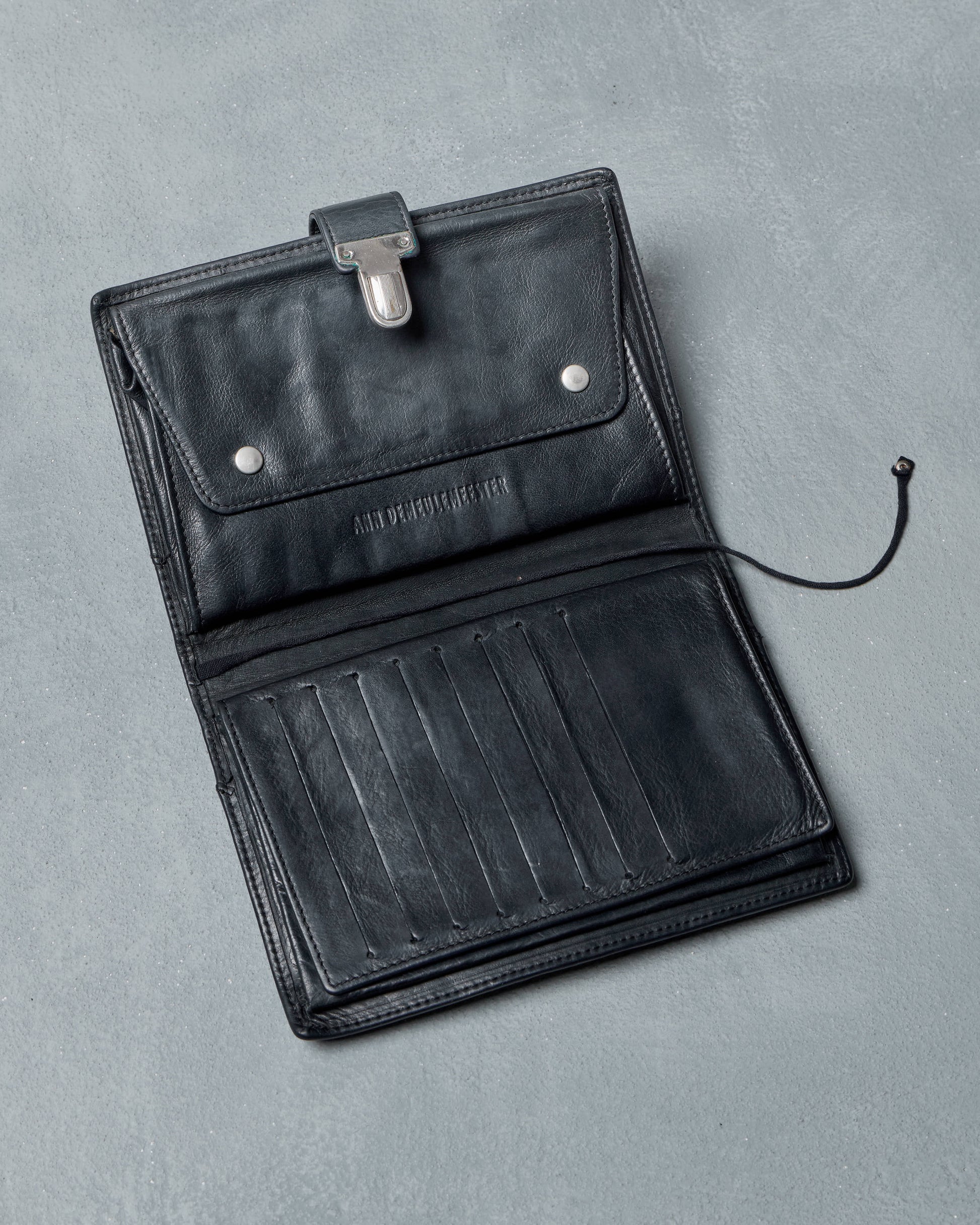 Black leather Ann Demeulemeester travel wallet on a gray background