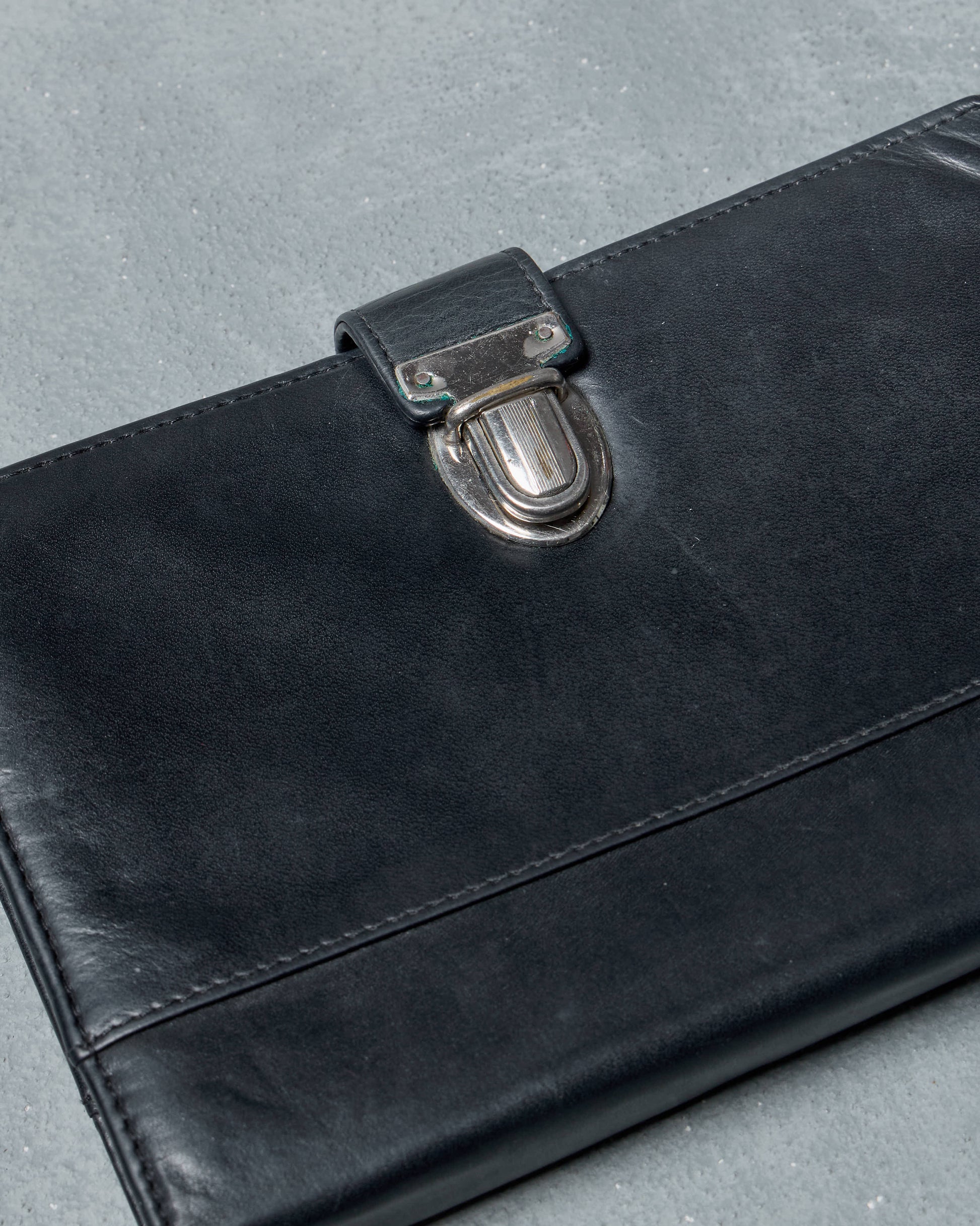 Black leather Ann Demeulemeester travel wallet with a clasp on a gray surface