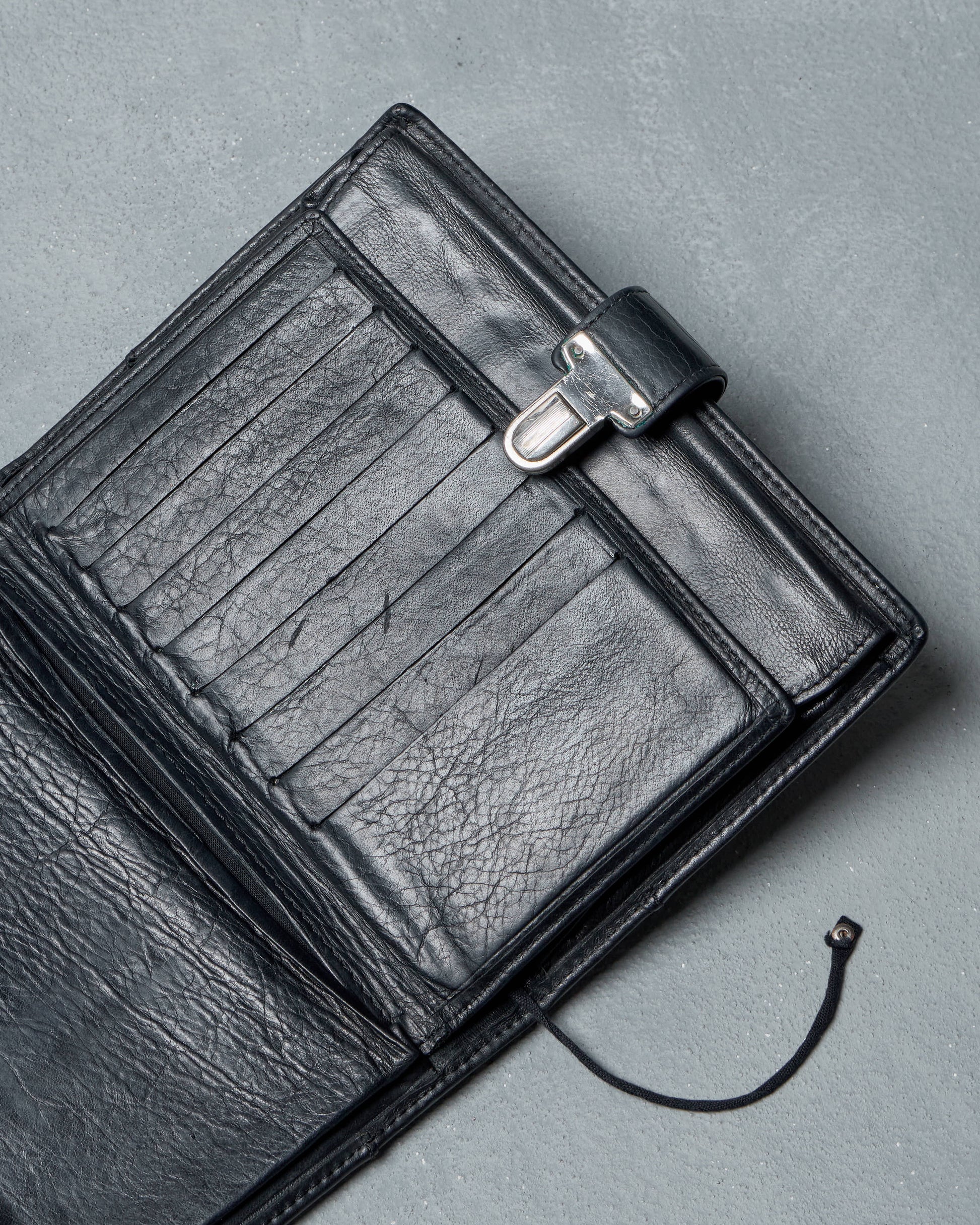 Black leather Ann Demeulemeester travel wallet on a gray background