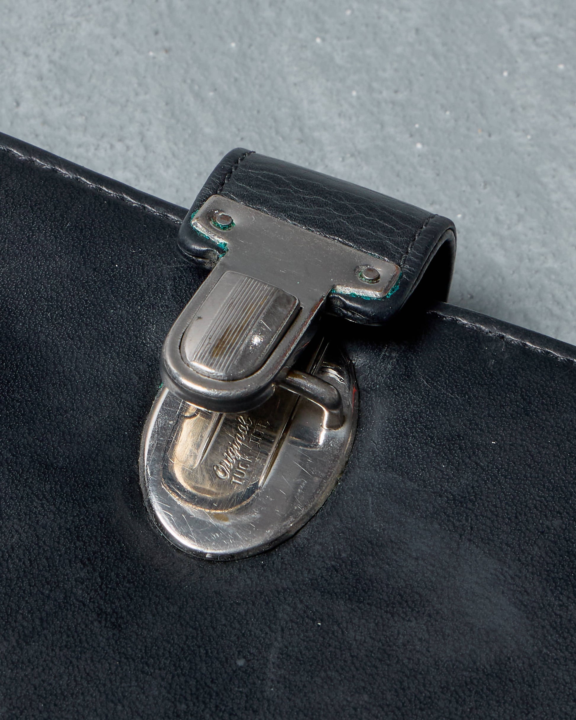 Close-up of a black leather Ann Demeulemeester travel wallet with a silver clasp on a gray background