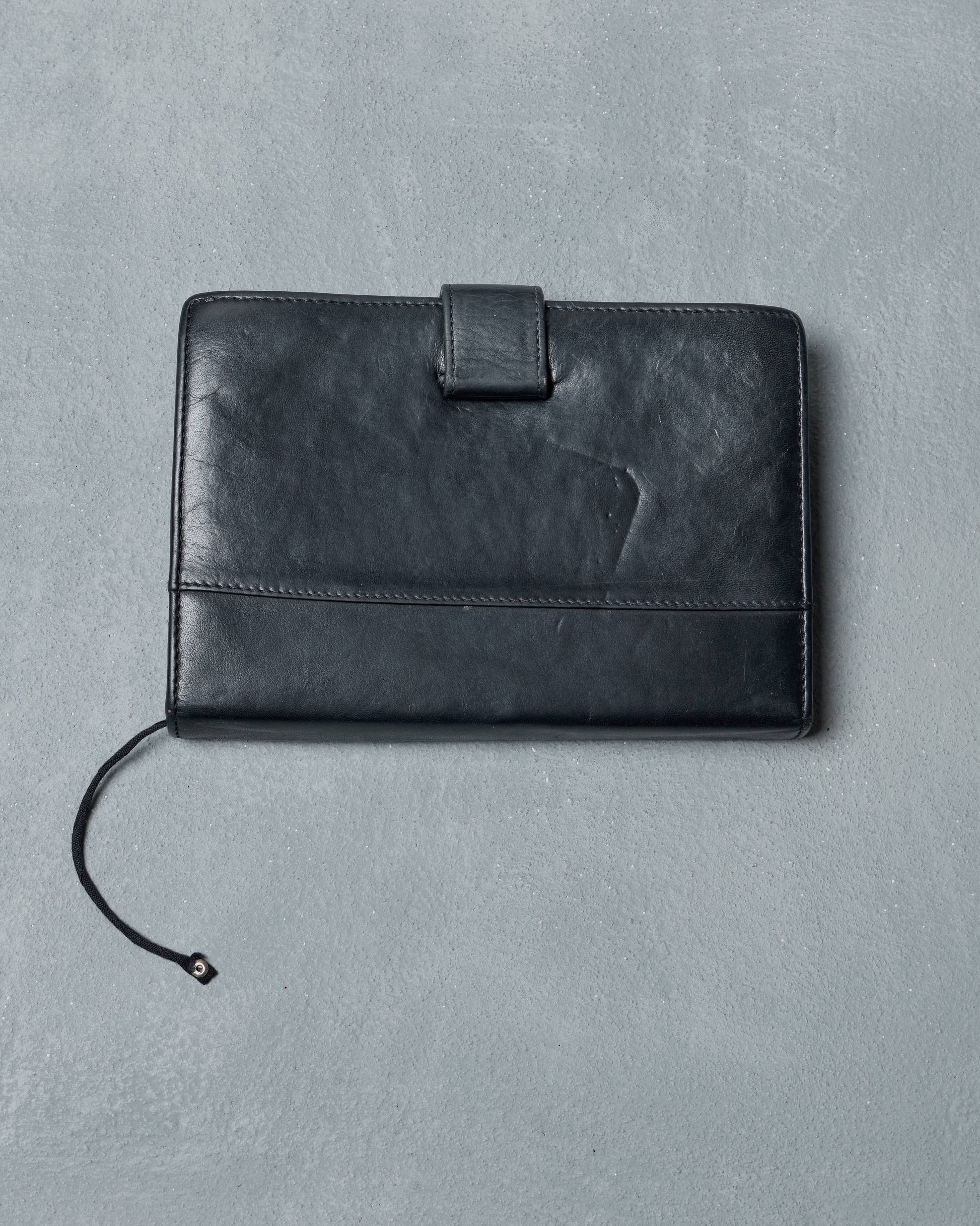 Black leather Ann Demeuelemeester travel wallet on a gray background