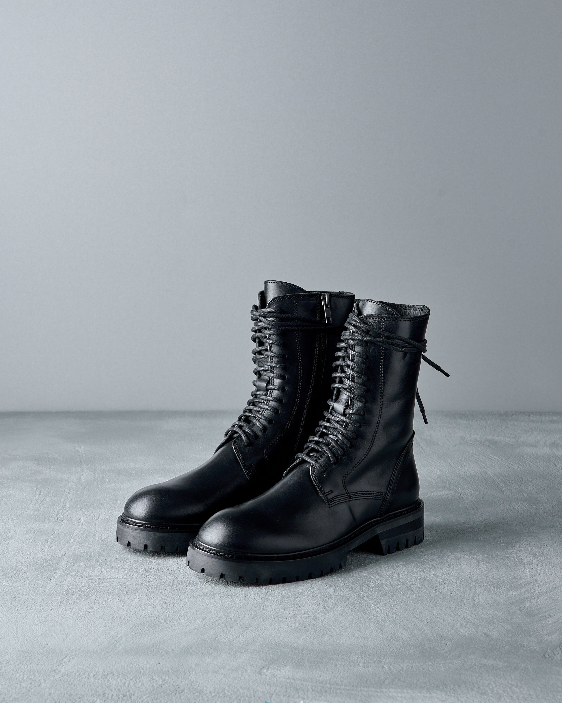 Pair of black leather Ann Demeulemeester boots on a gray surface with a gray background