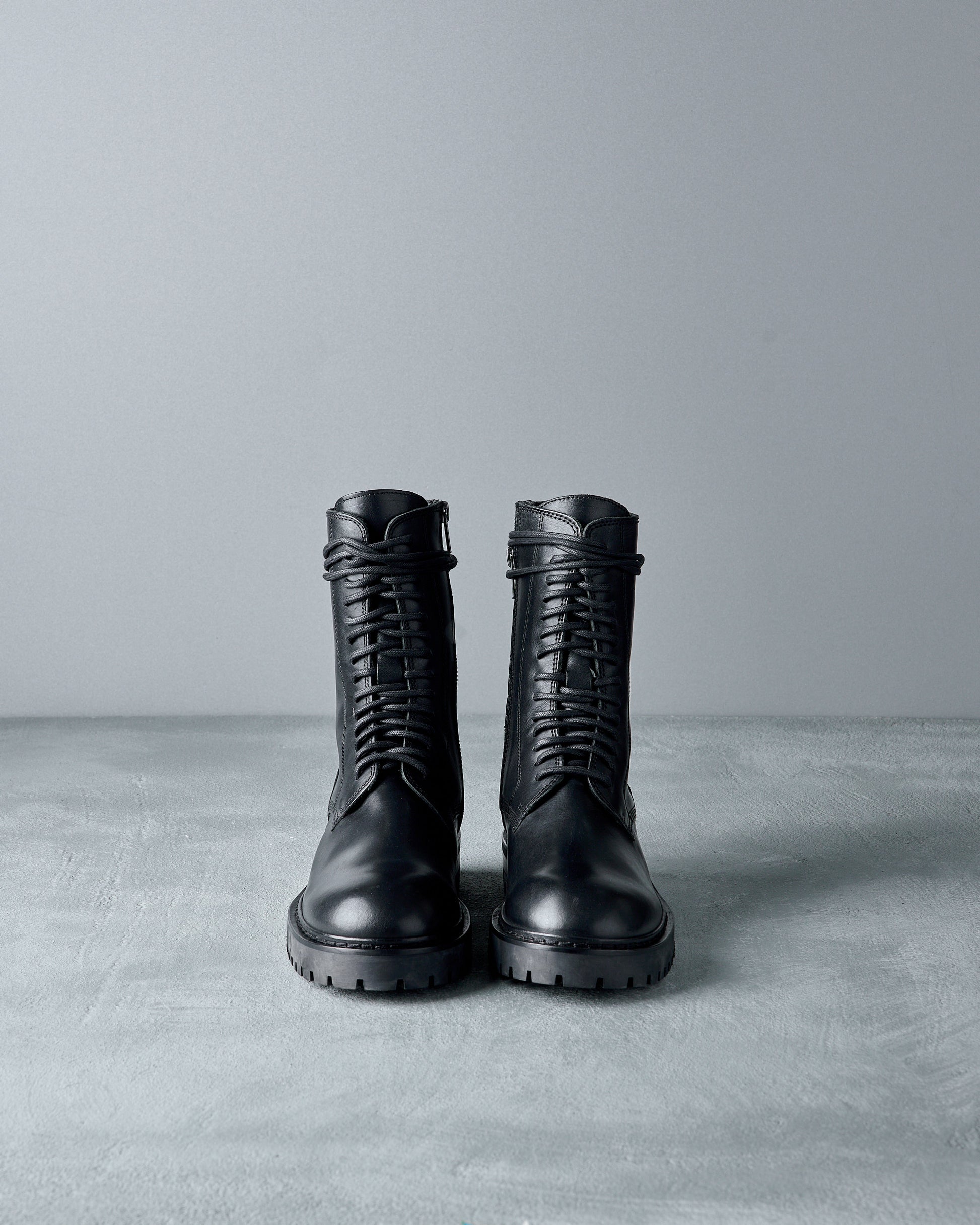 Pair of black leather Ann Demeulemeester  boots on a gray surface with a gray background