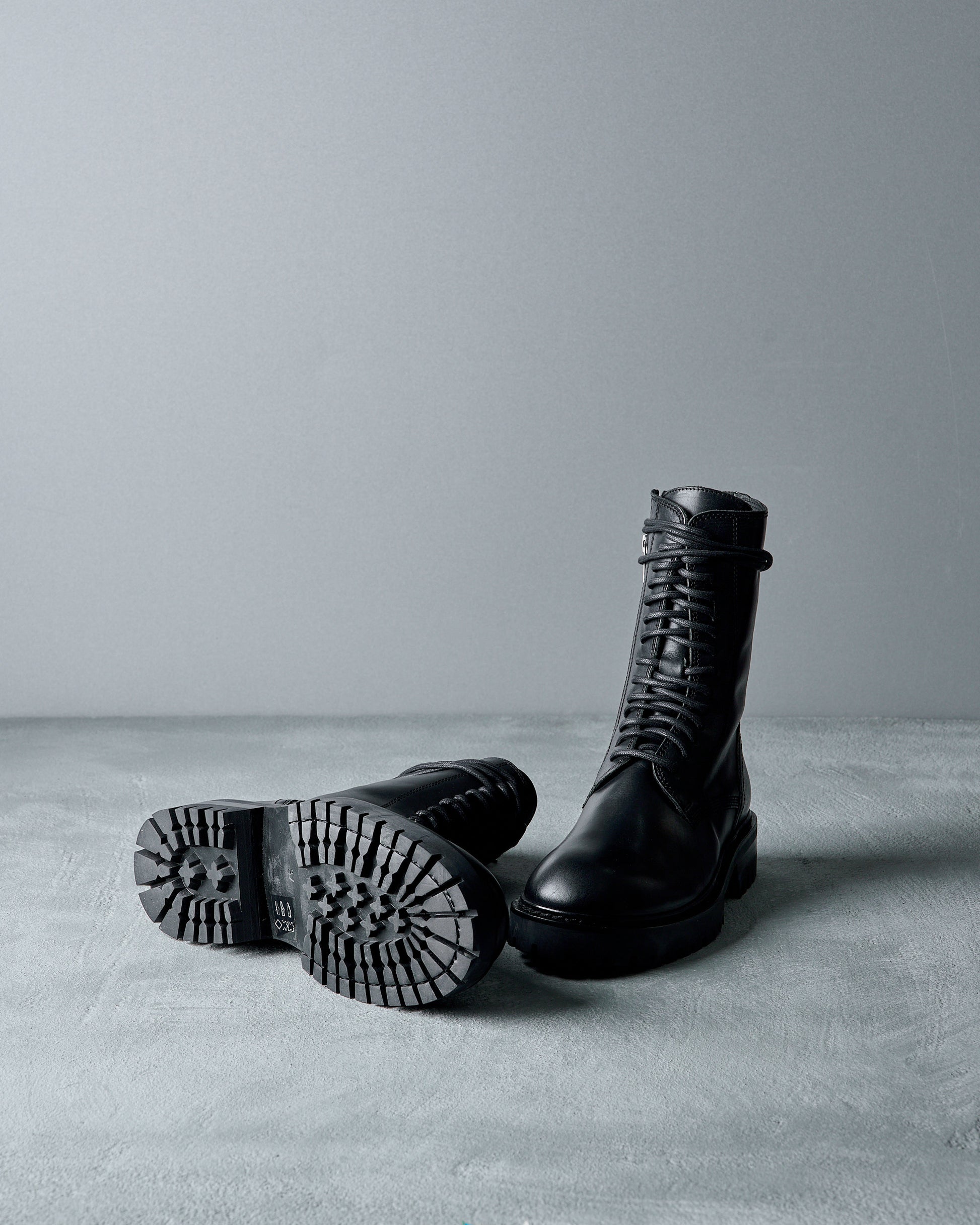Black leather Ann Demeulemeester  boots on a gray surface with a neutral background