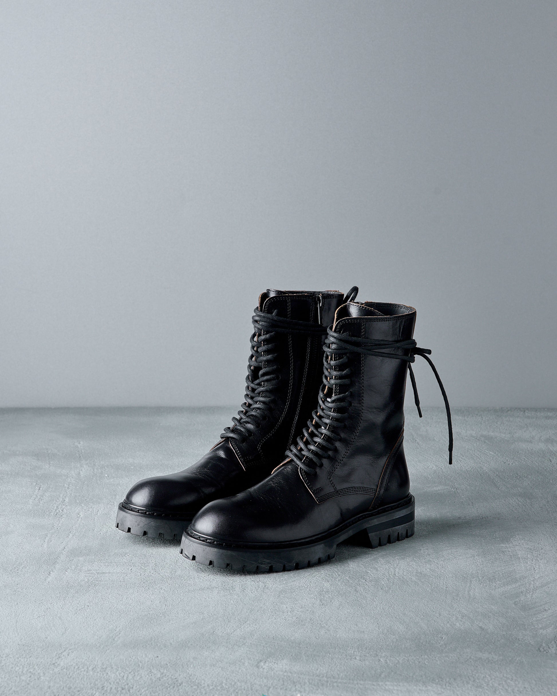 Pair of black leather Ann Demeulemeester boots on a gray surface with a neutral background