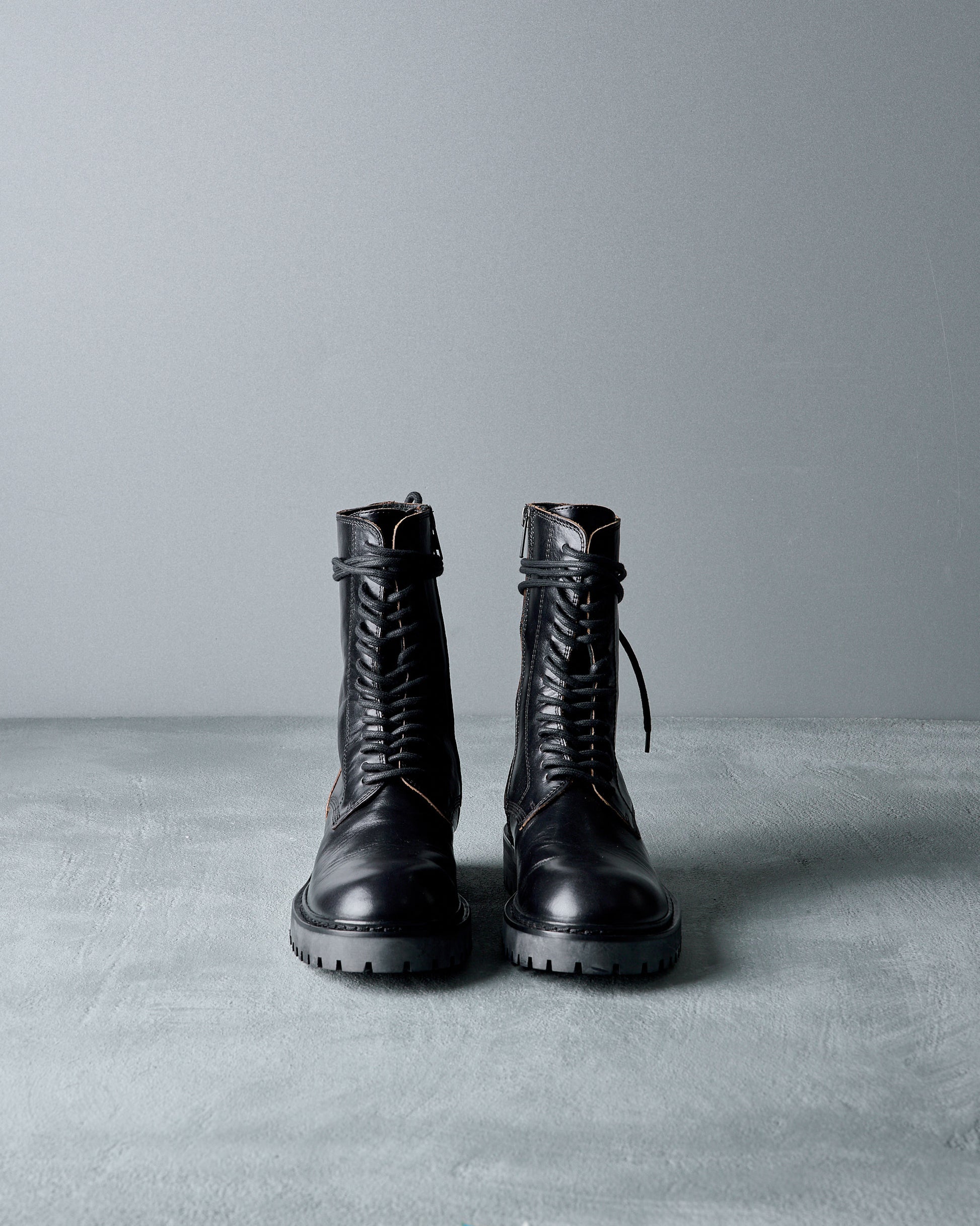 Pair of black leather Ann Demeulemeester  boots on a gray surface with a gray background