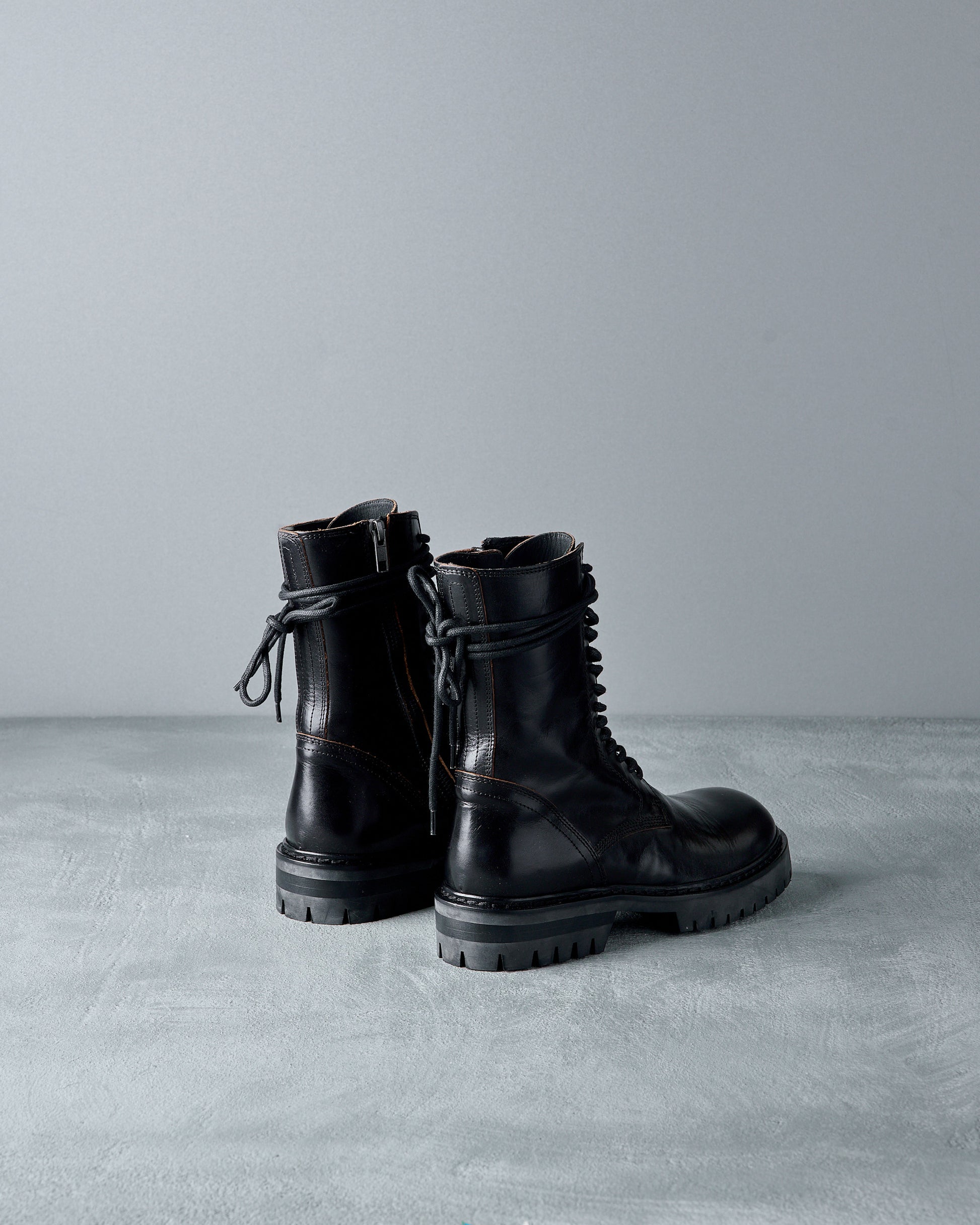 Pair of black leather Ann Demeulemeester boots on a gray surface with a light gray background