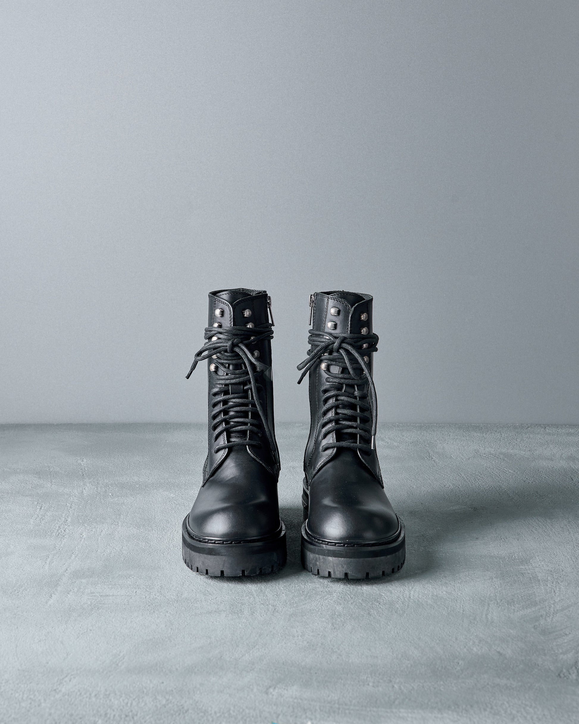 Pair of black leather Ann Demeulemeester  boots on a grey background