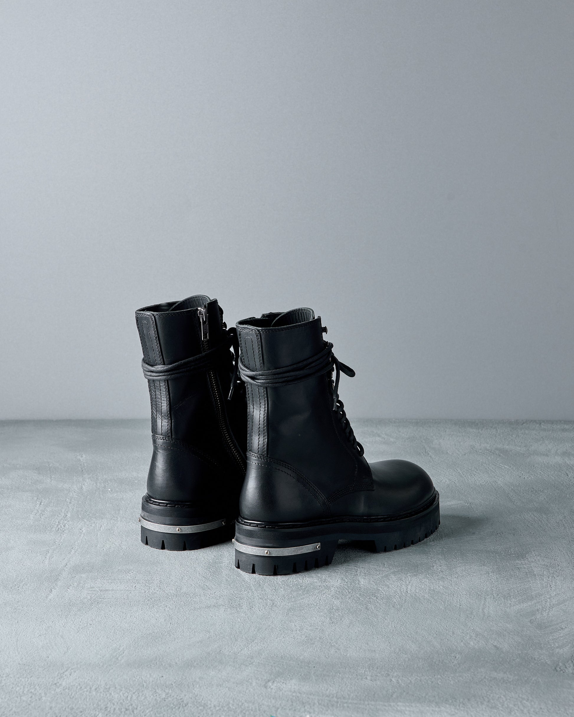 Pair of black leather Ann Demeulemeester boots on a grey surface with a neutral background