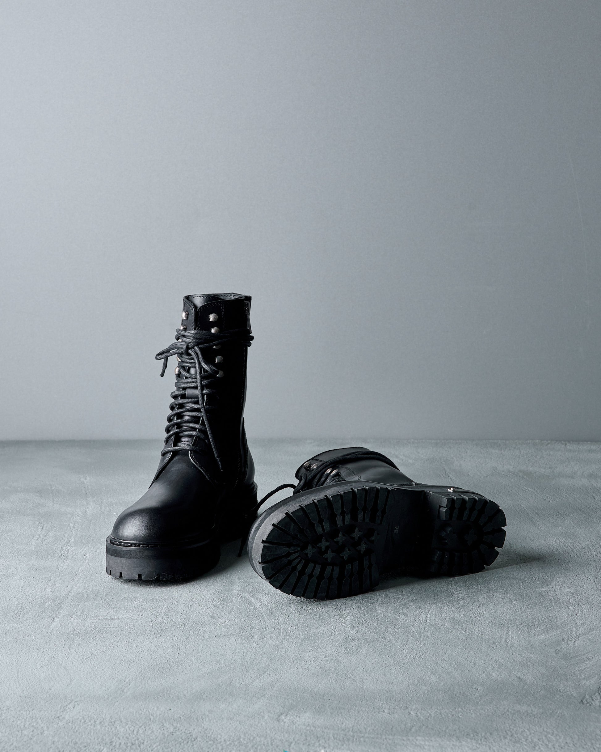 Pair of black leather Ann Demeulemeester boots on a grey surface with a grey background