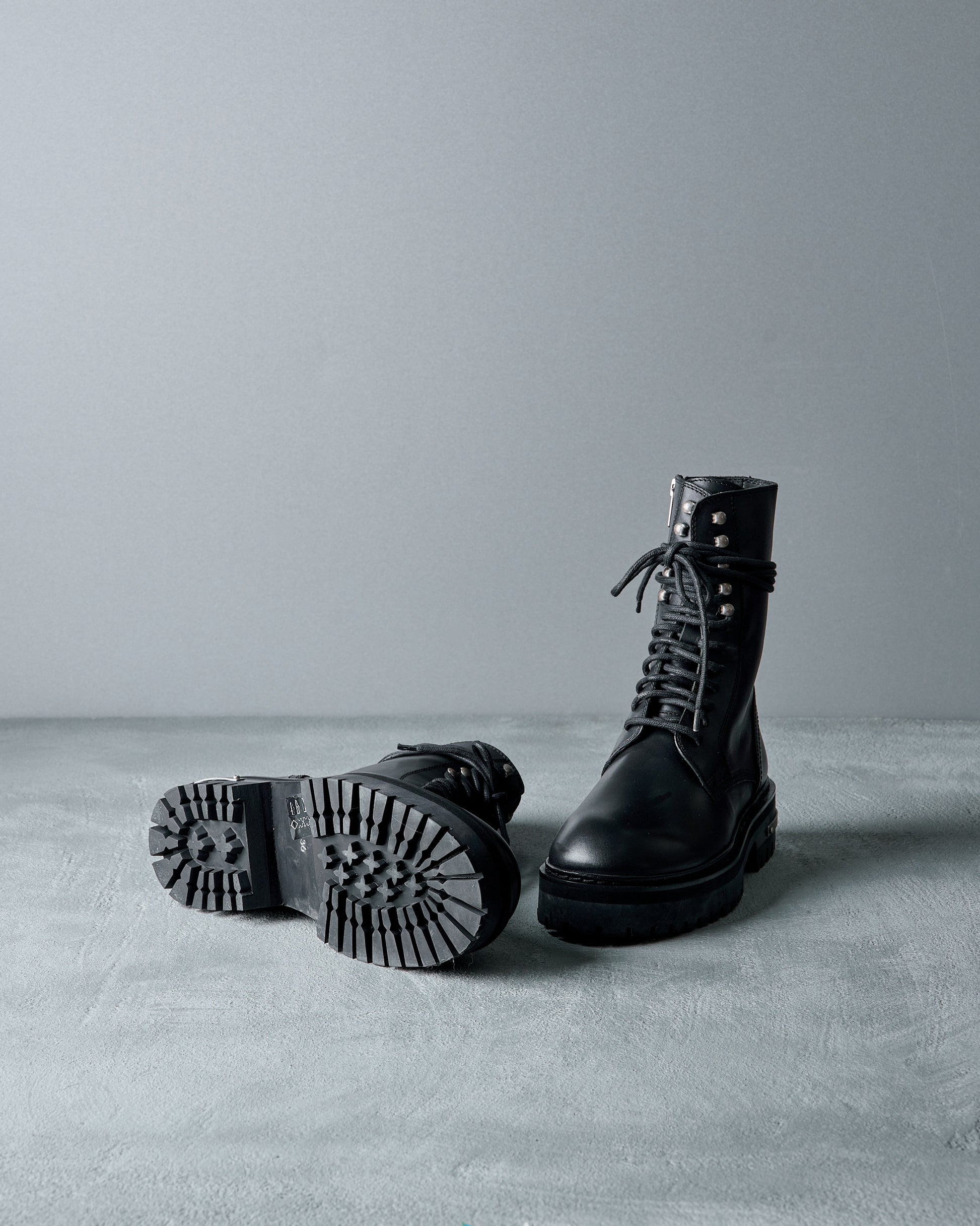 Pair of black leather AnnDemeulemeester boots on a gray surface with a neutral background